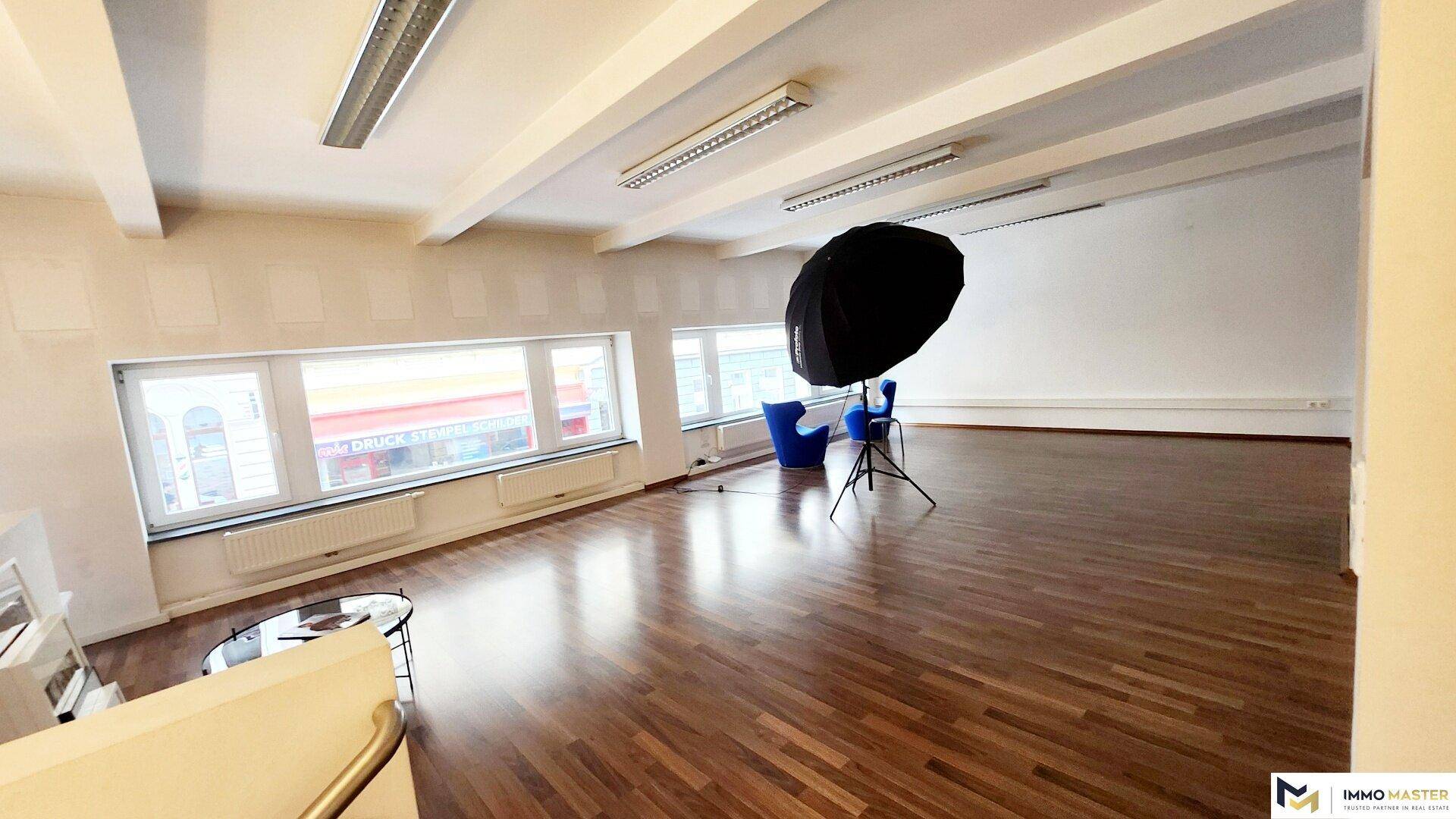 Vielseitiger Bürobereich mit Holzboden, großen Fenstern und professioneller Fotoausrüstung für kreative Projekte.