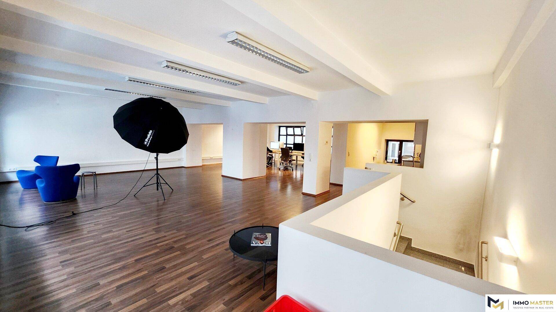 Großzügiger Büroraum mit Holzboden, Treppenabgang und Blick in weitere offene Arbeitsbereiche.