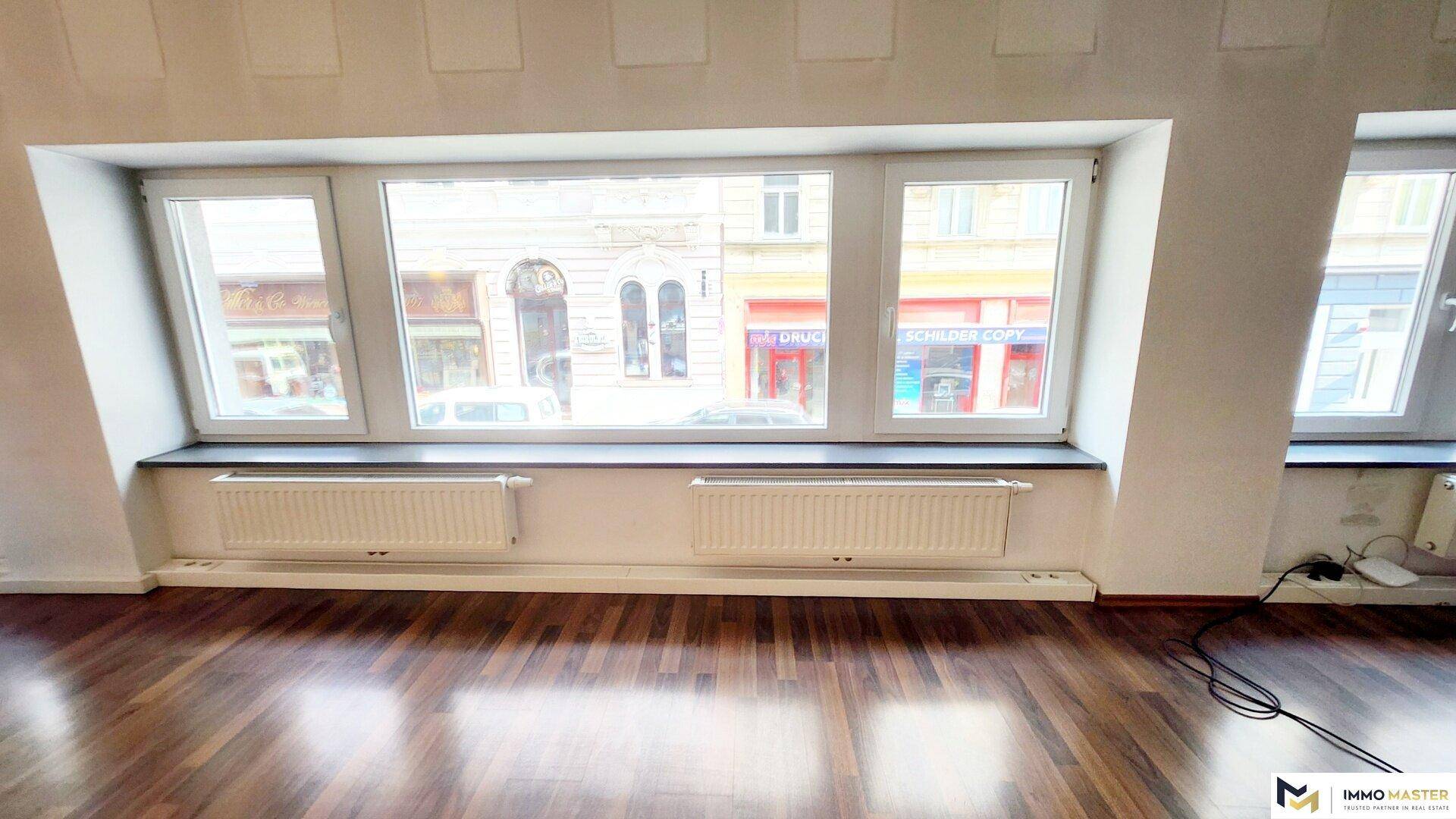 Detailansicht eines Fensters in einem Büroraum mit Holzboden und Heizkörpern darunter.