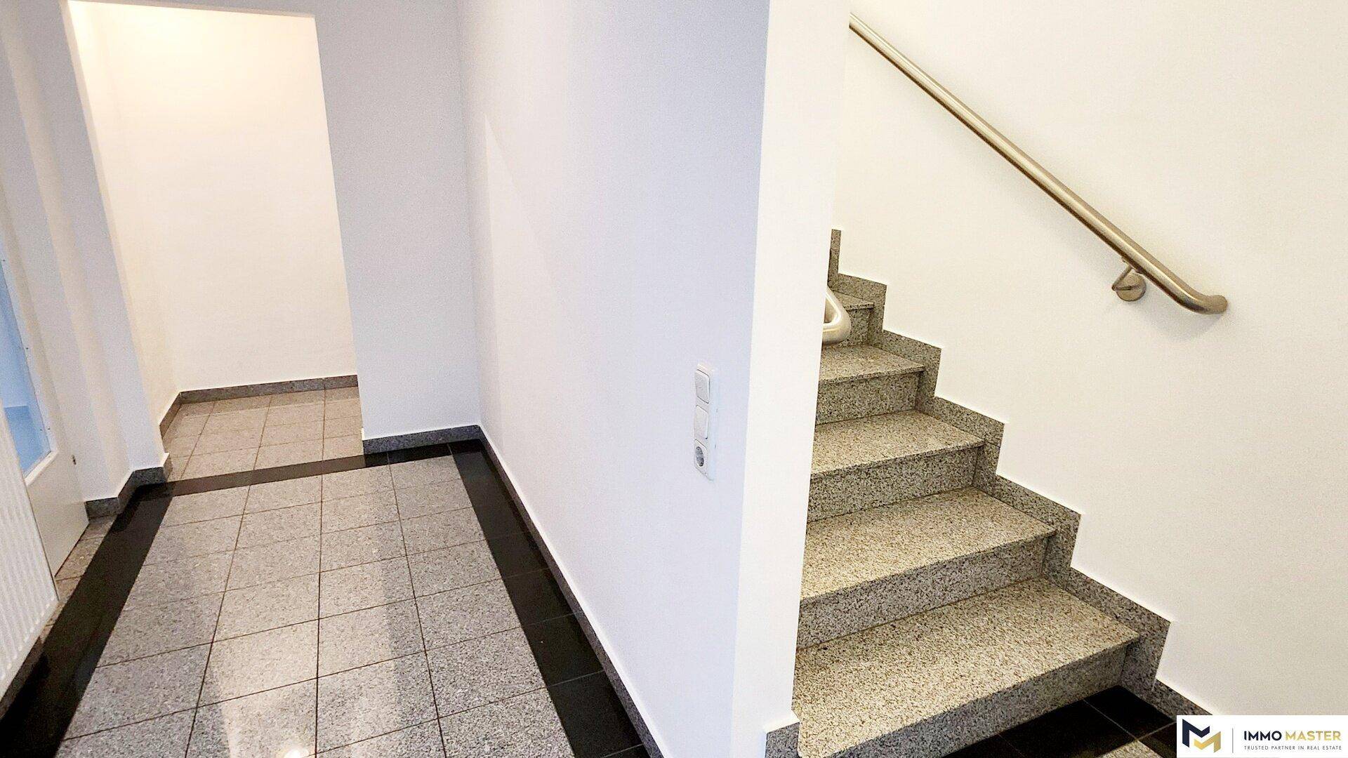 Treppenhaus mit Granitfliesen und einem stabilen Handlauf, der zu den oberen Etagen führt.