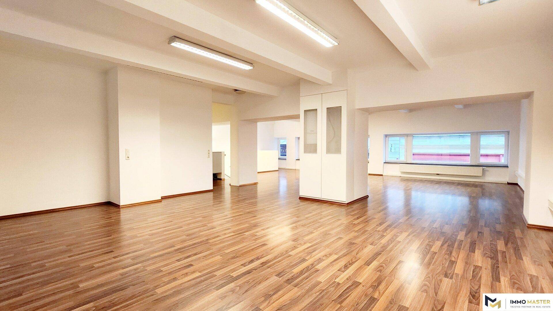 Offener Bürobereich mit Holzboden und integriertem Schrank, der verschiedene Arbeitszonen funktional verbindet.