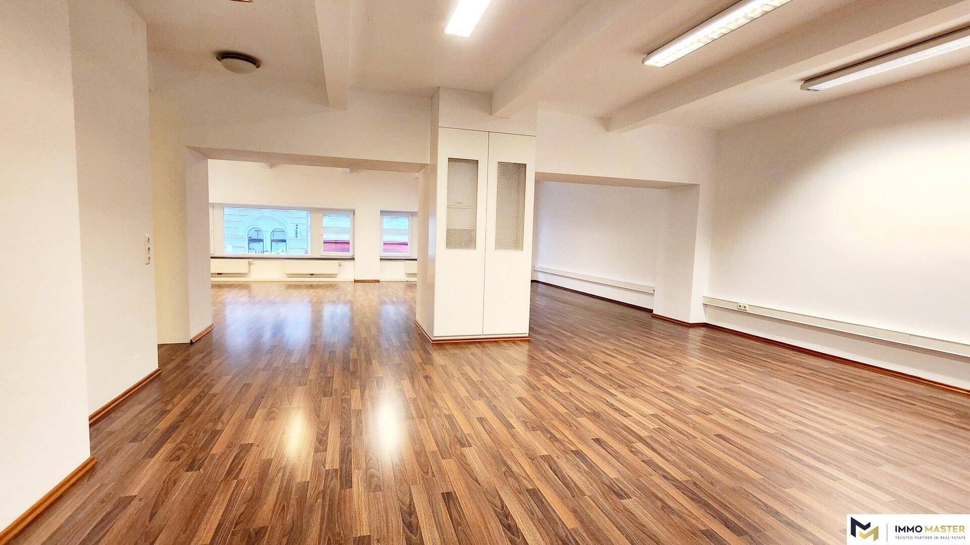 Weitläufiger Büroraum mit Holzboden und einem zentralen Einbauschrank, der den offenen Raum strukturiert.