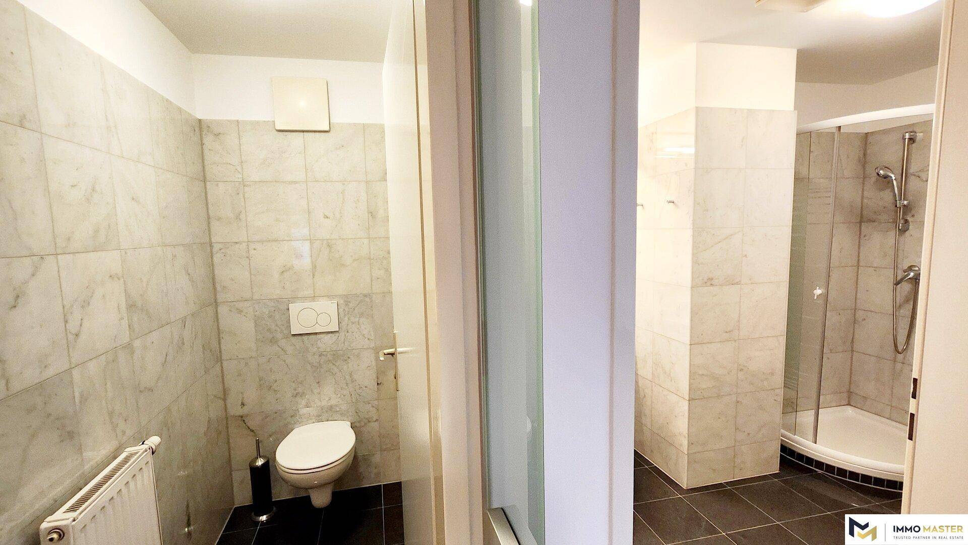Badezimmer mit Marmorfliesen, Toilette und separater Duschkabine, ausgestattet mit Abluftventilator.