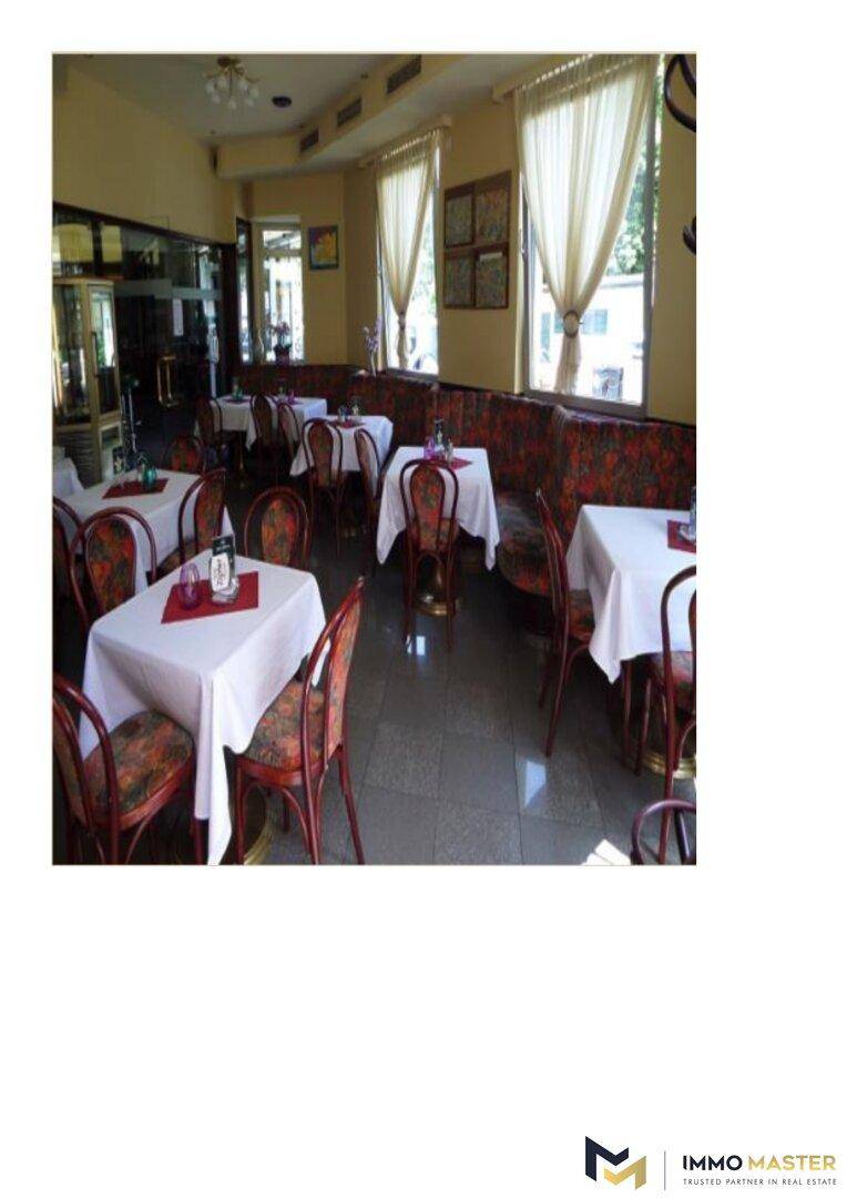 Geräumiger Restaurantinnenraum mit mehreren Tischen, gepolsterten Bänken und großen Fenstern.