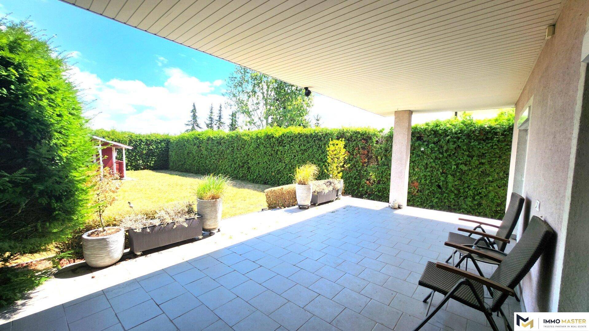 Geräumige, überdachte Terrasse mit Blick auf den sonnigen Garten und die grüne Hecke.