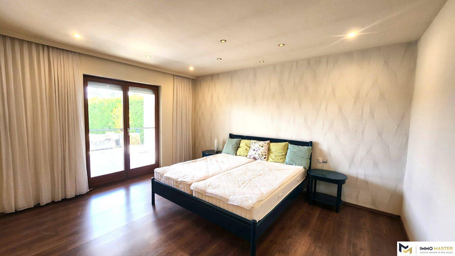 Geräumiges Schlafzimmer mit Holzboden, Doppelbett und großen Fenstertüren zum Garten.