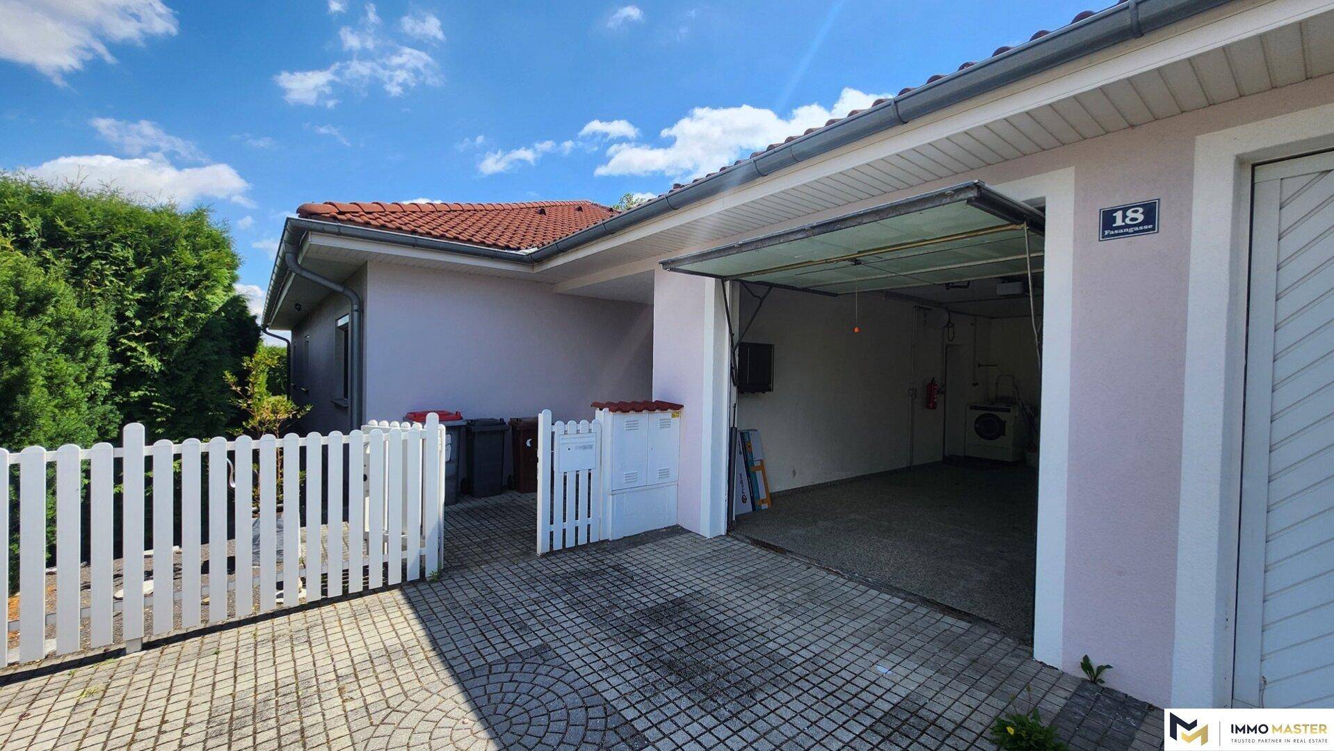 Garagenzufahrt mit offenem Tor und kleinem Vorgartenbereich mit Zaun.