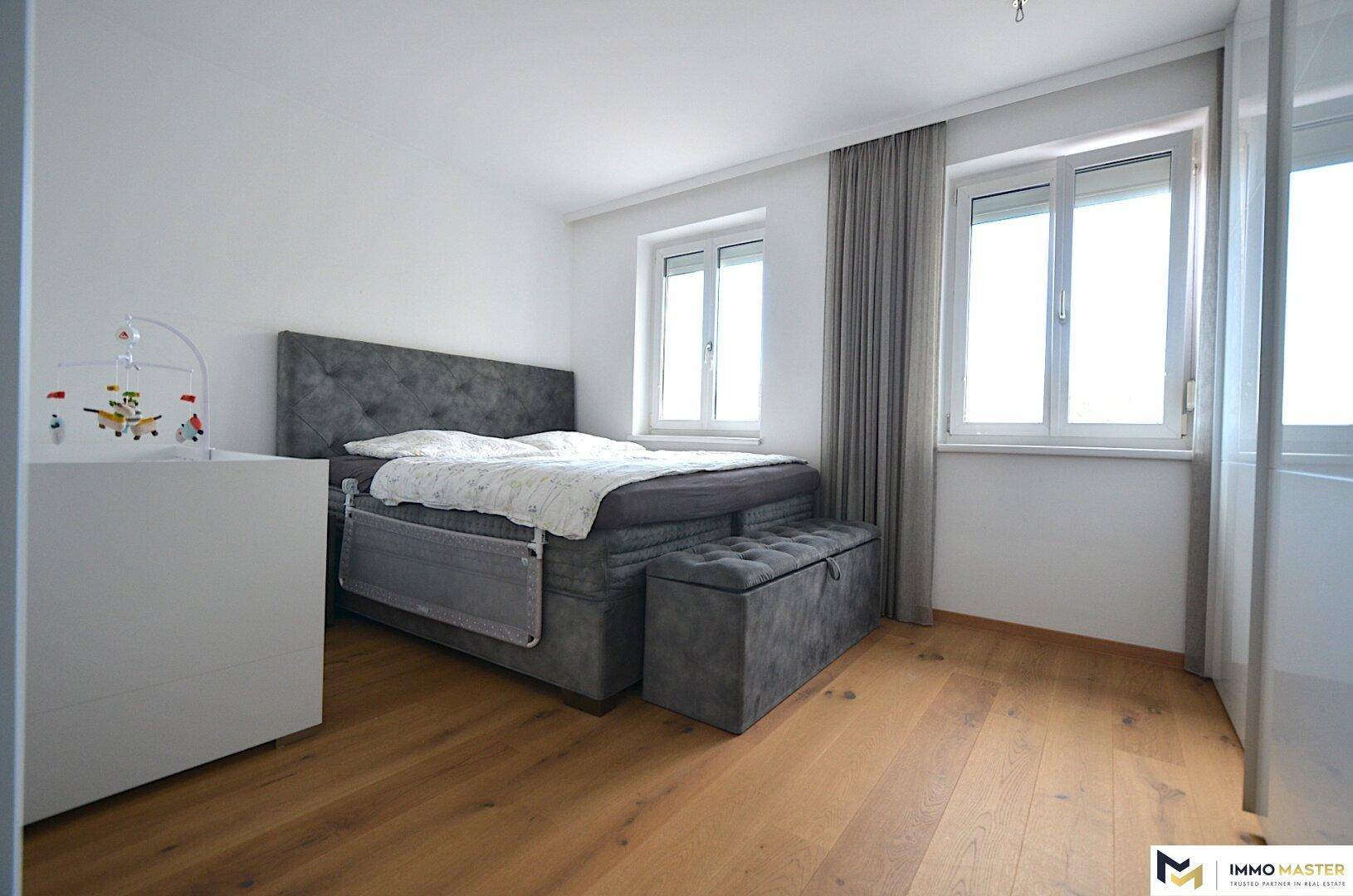 Ruhiges Schlafzimmer mit großem Doppelbett, Holzboden und viel natürlichem Licht durch zwei Fenster.
