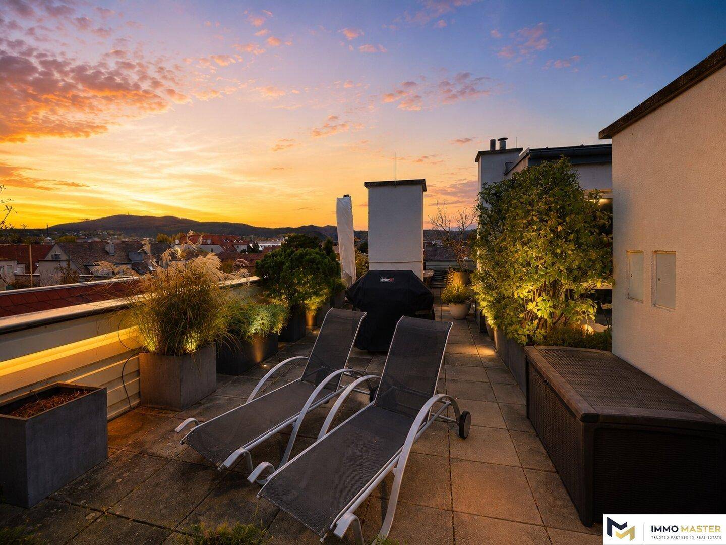 Dachterrasse bei Sonnenuntergang mit Liegestühlen, Grill und stimmungsvollem Blick auf die Berge.