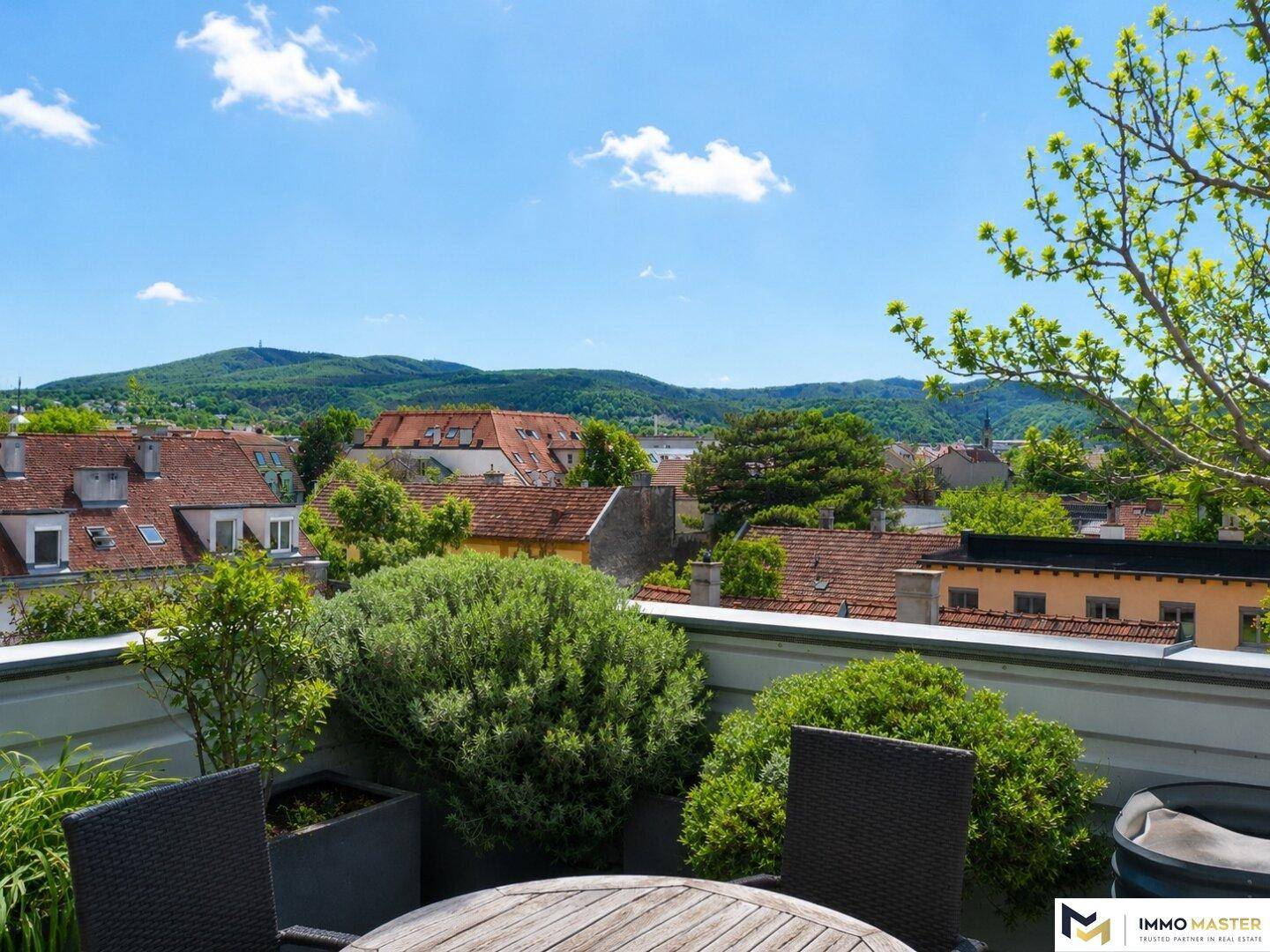 Panoramablick von der Dachterrasse über die Dächer der Stadt und die grünen Berge in der Ferne.