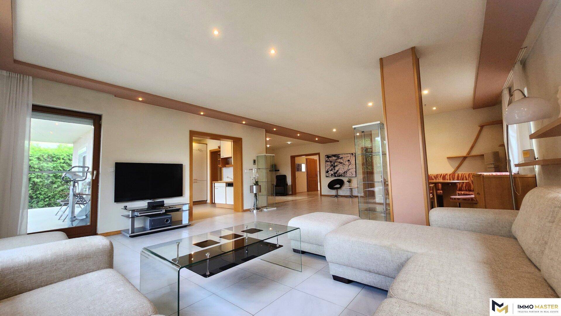 Heller offener Wohnbereich mit beigem Sofa, Esstisch und Zugang zu einem Balkon.