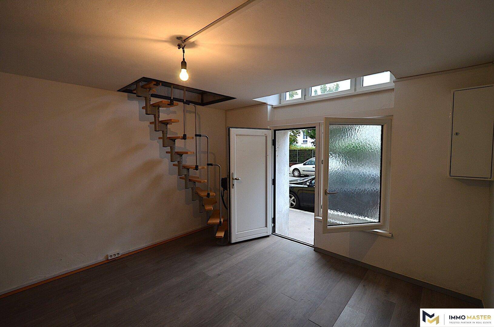 Heller Wohnraum mit einer modernen Wendeltreppe, dunklem Laminatboden und direktem Zugang nach draußen.