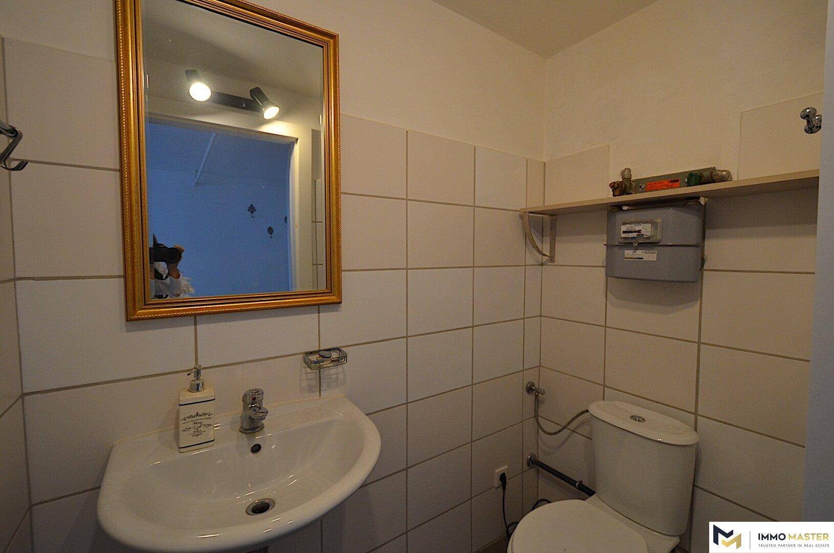Kleines Gäste-WC mit weiß gefliesten Wänden, einem Waschbecken, einem Spiegel und einer Toilette.