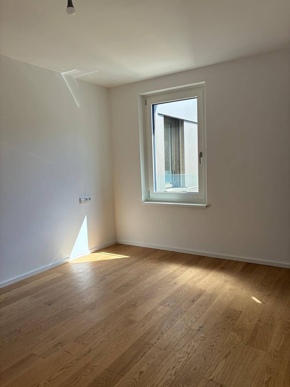 Heller, leerer Raum mit weißen Wänden und einem Fenster, das viel Tageslicht hereinlässt.