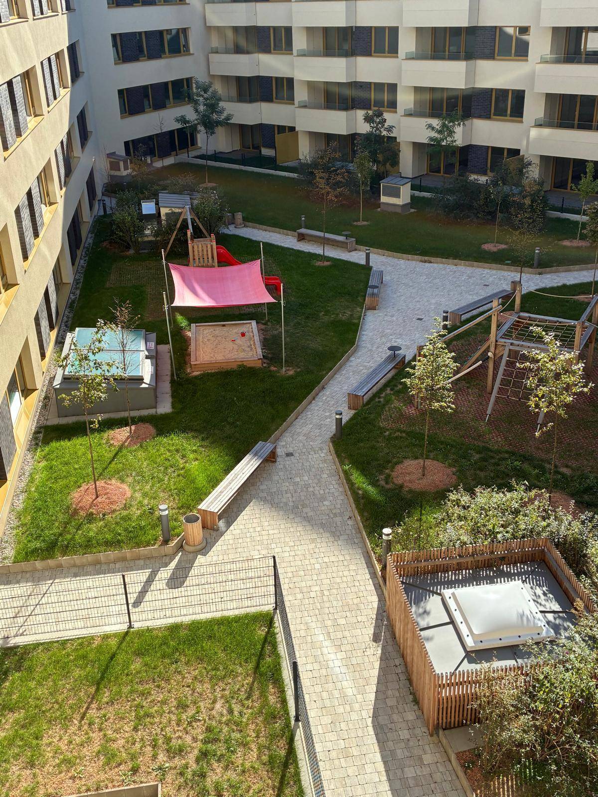 Gemeinschaftlicher Innenhofgarten mit Spielplatz, Sitzbänken und gepflegten Grünflächen zwischen den Gebäuden.