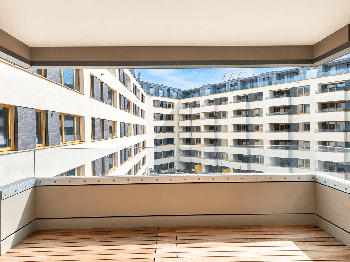 Balkon mit Holzboden und Glasbrüstung bietet Blick auf den Innenhof des modernen Gebäudekomplexes.