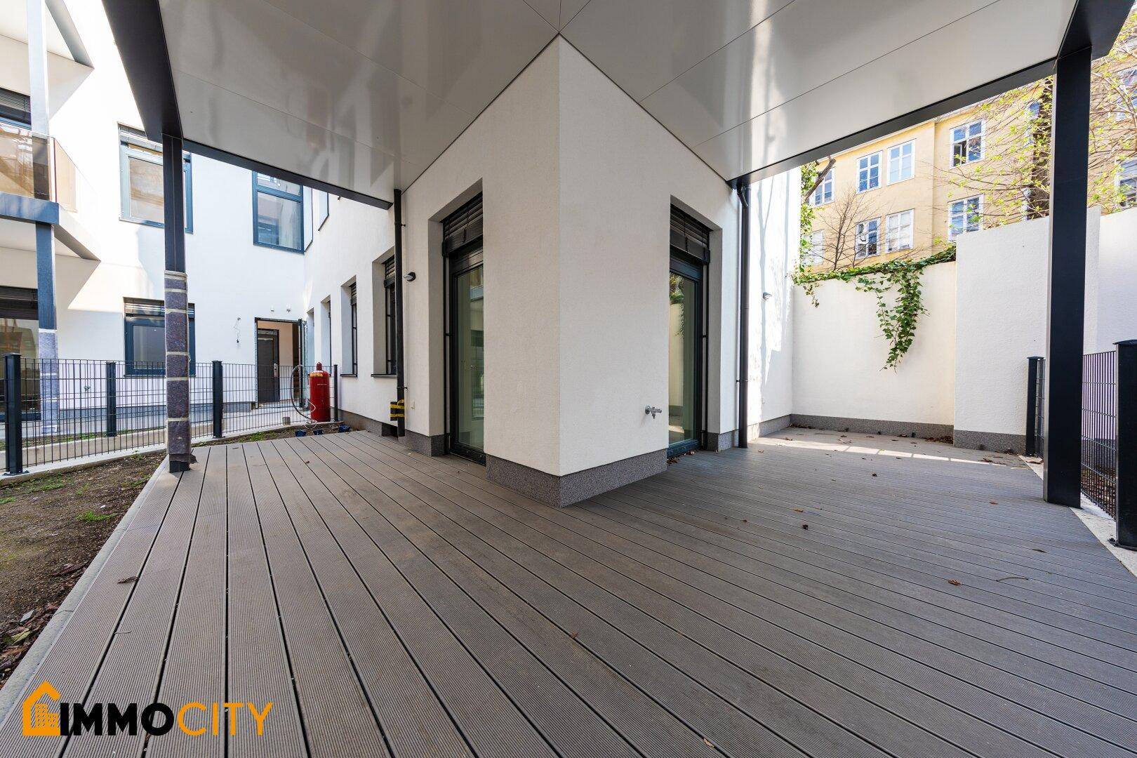 Große, überdachte Terrasse mit modernem Holzdeck und Zugang zum Gebäude.