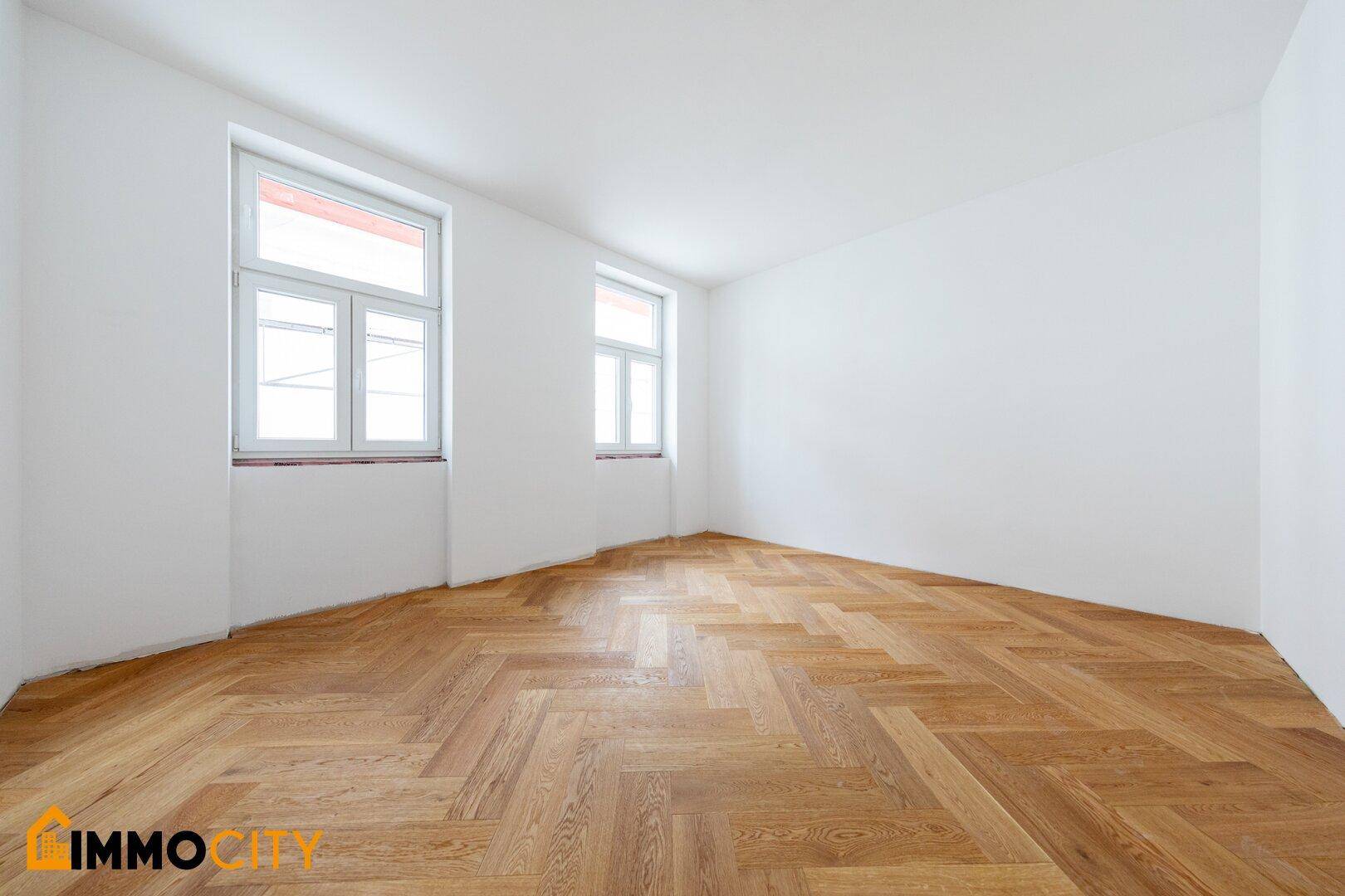 Heller, leerer Raum mit Fischgrätparkett und zwei Fenstern, ideal als Schlafzimmer oder Büro.