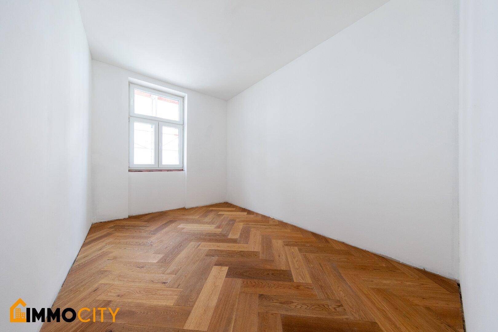 Heller, leerer Raum mit Fischgrätparkett und einem Fenster, ideal als Schlafzimmer oder Kinderzimmer.