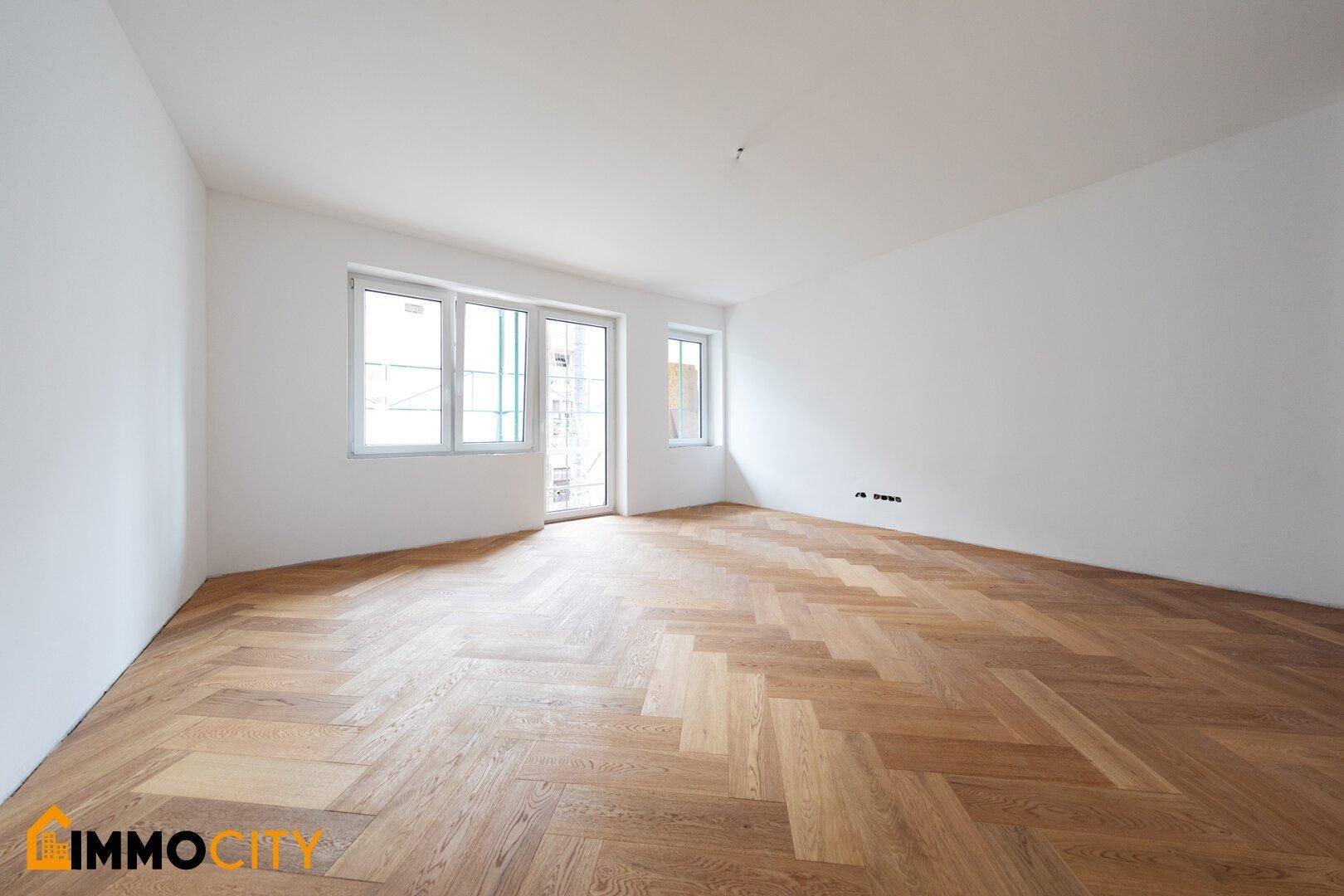 Geräumiger, heller Raum mit Fischgrätparkett und Fenstertür zum potenziellen Balkon oder Terrasse.