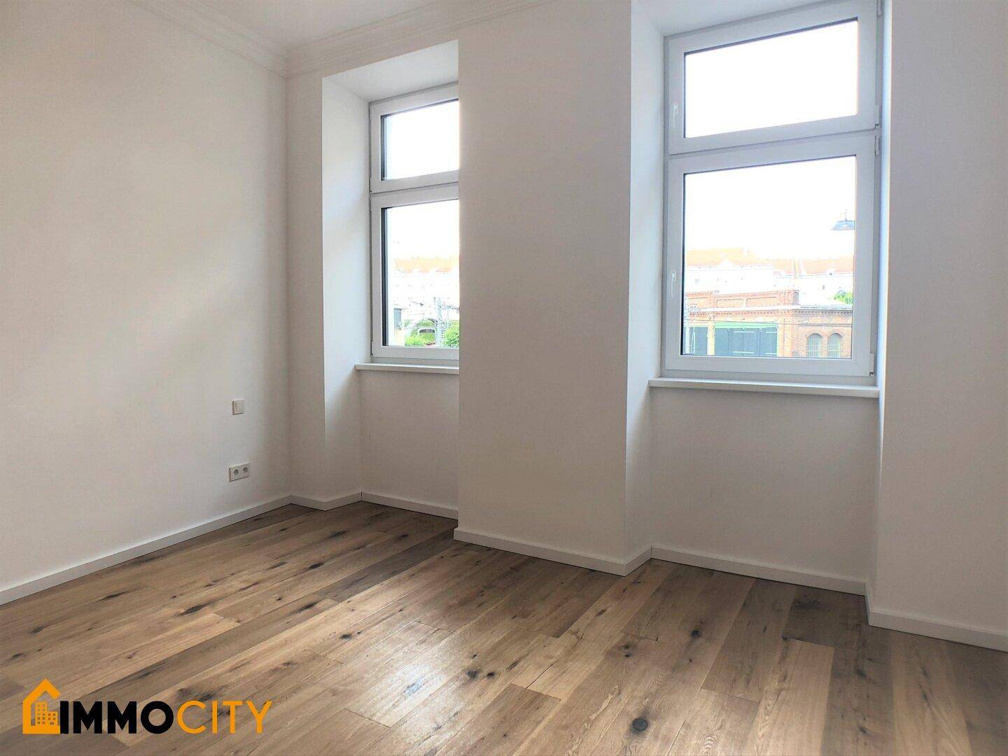 Lichtdurchfluteter Raum mit neuem Holzboden und zwei großen Fenstern, ideal für Wohnzwecke.