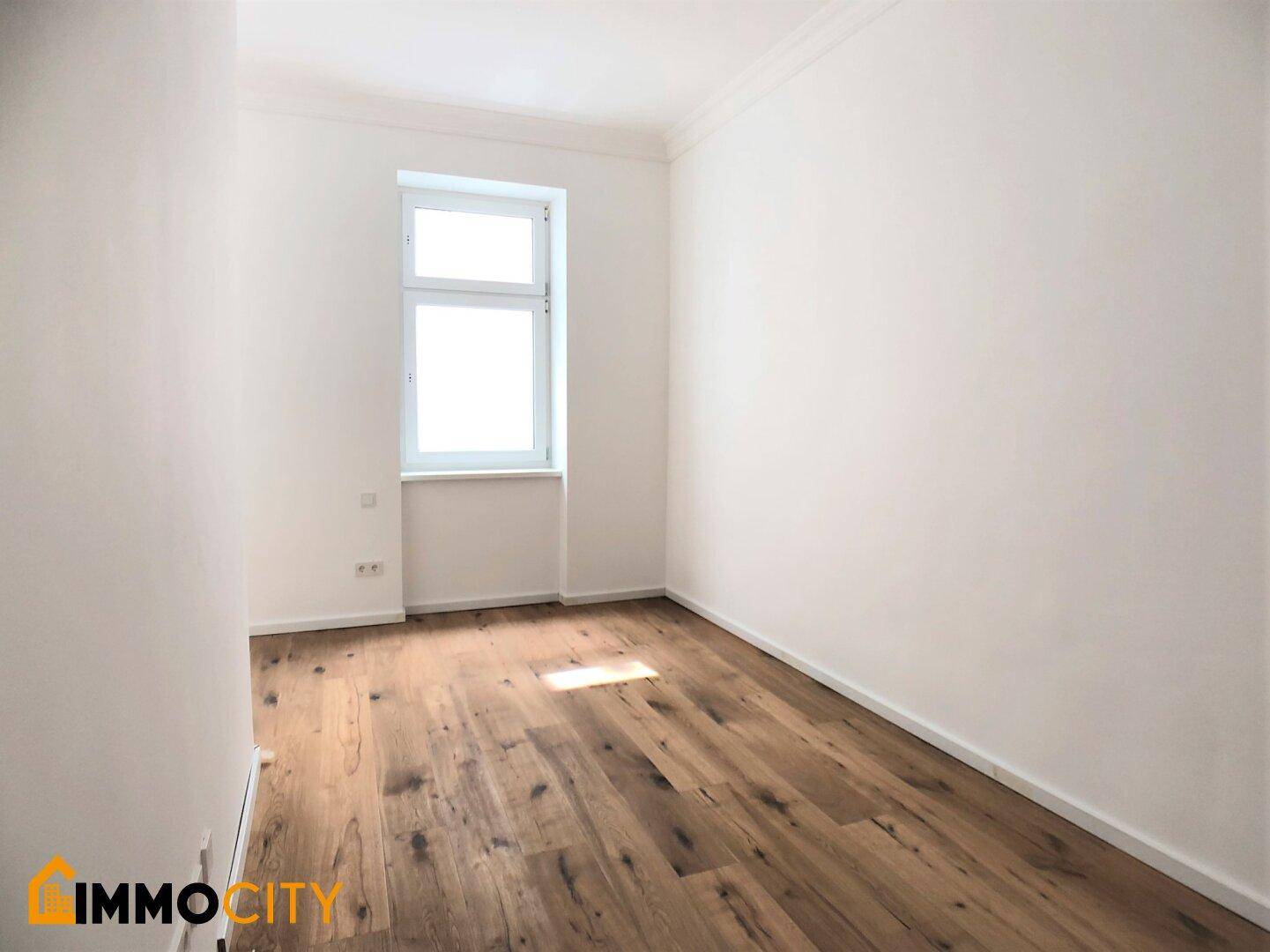 Gemütliches Zimmer mit Holzboden und einem Fenster, das viel Tageslicht hereinlässt.