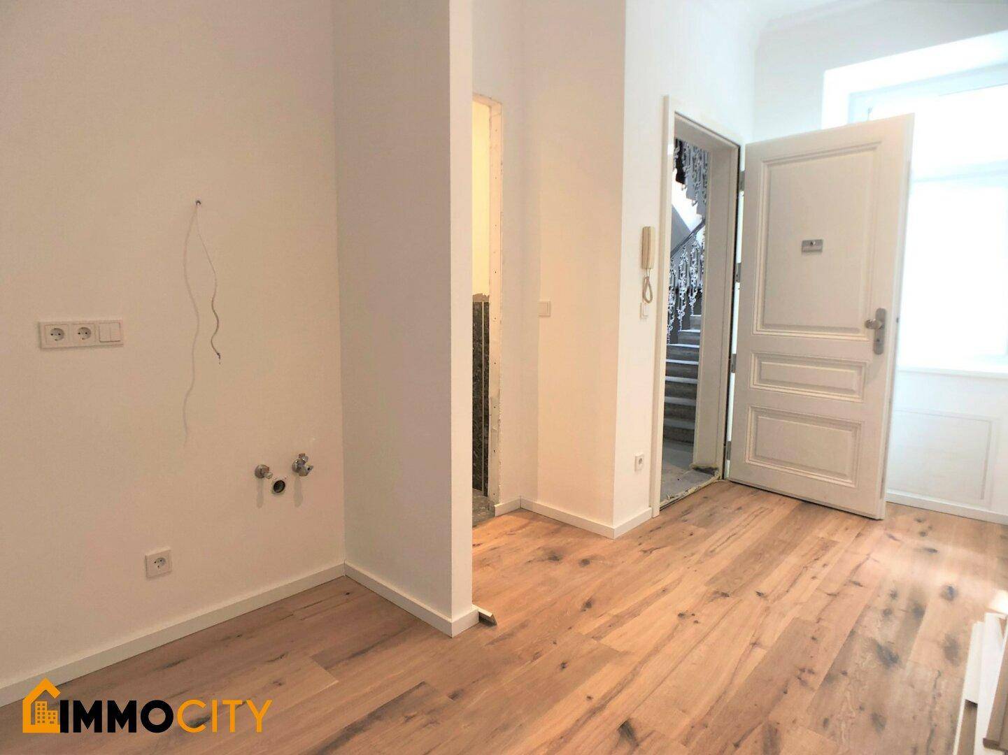 Bereich mit Holzboden und Anschlüssen für eine mögliche Küchenzeile oder einen Hauswirtschaftsraum.