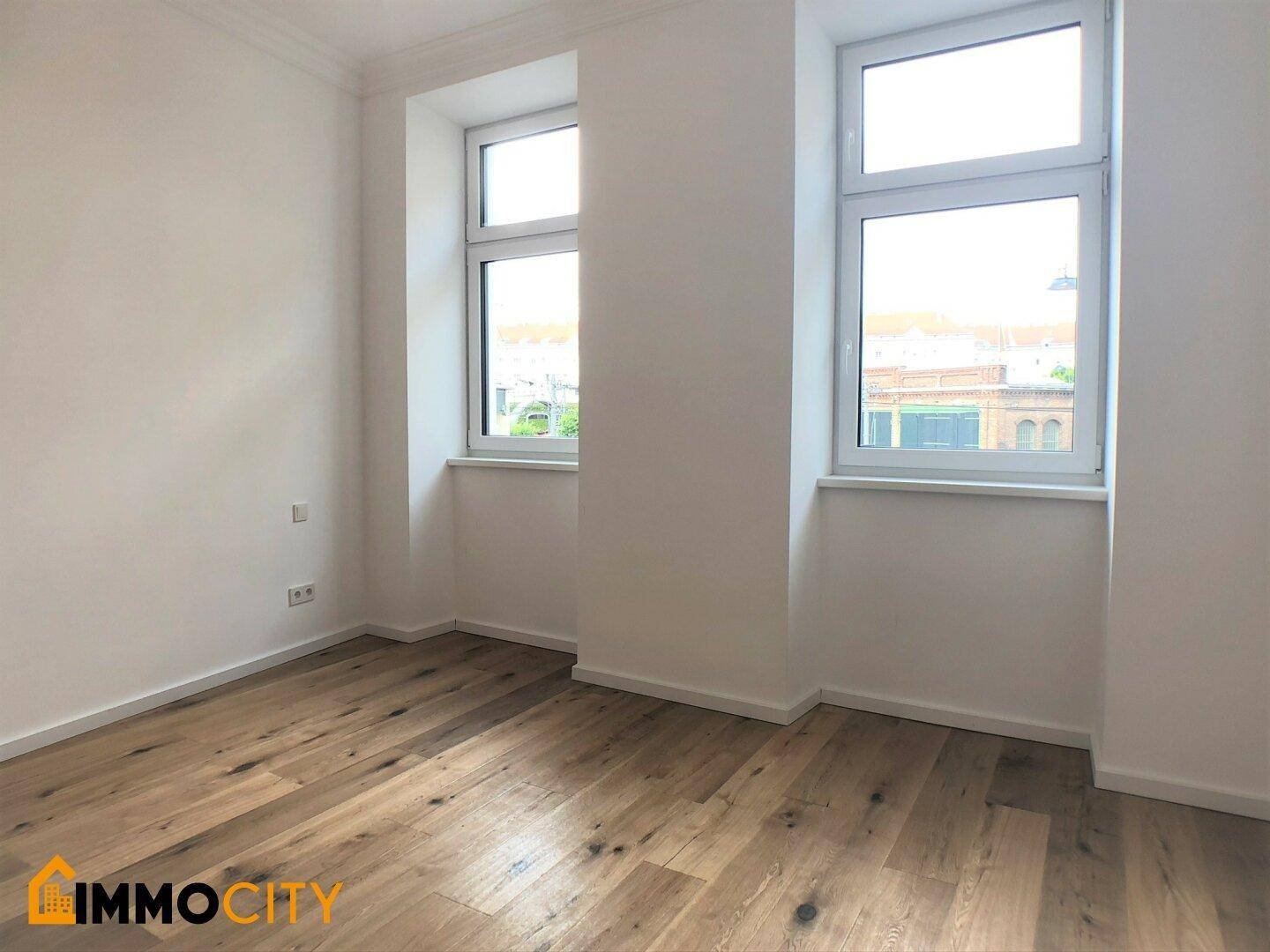Helles Schlafzimmer mit Holzboden und zwei Fenstern, bietet viel Tageslicht.