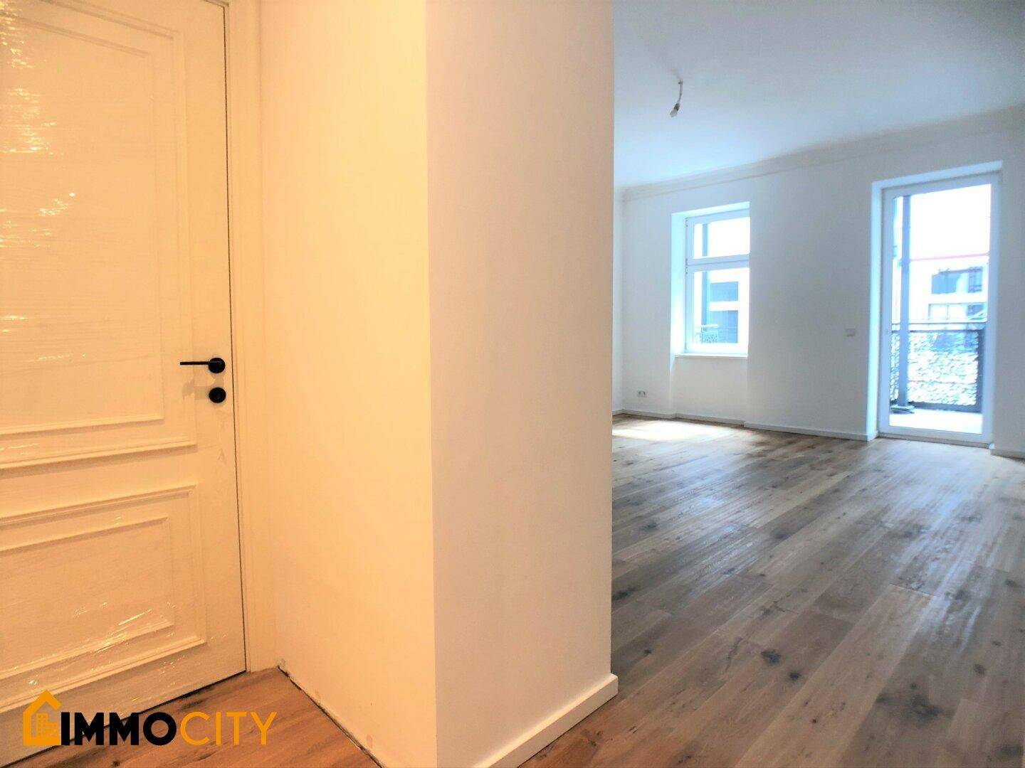 Helles Zimmer mit Holzboden und Zugang zu einem Balkon, ideal für Wohnzwecke.