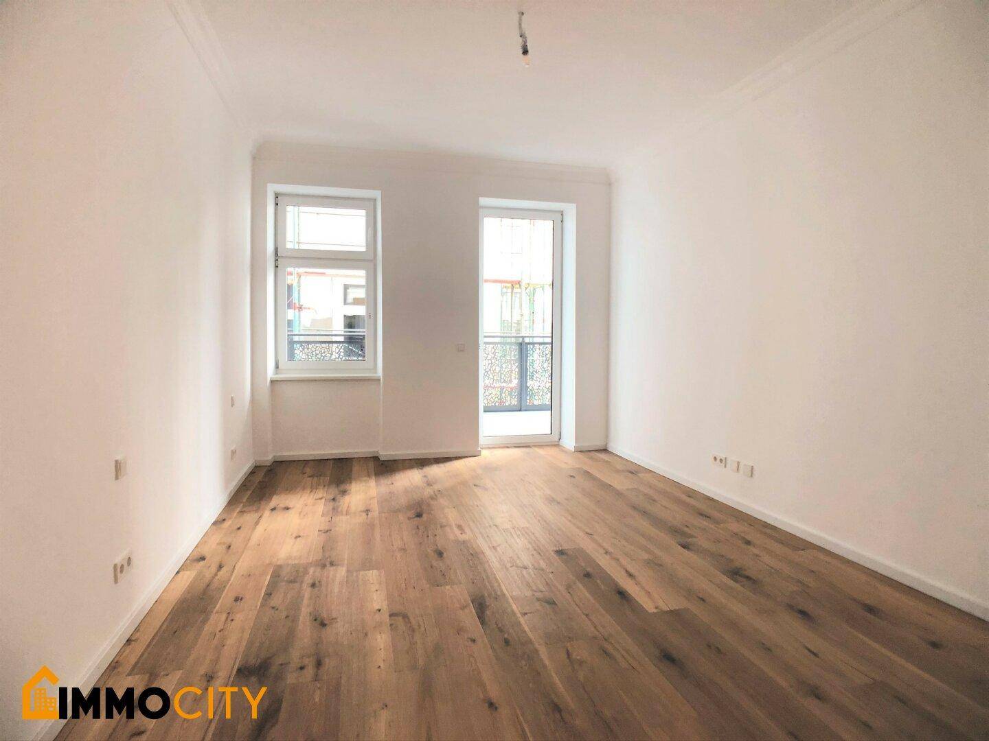 Geräumiges Zimmer mit Holzboden und Balkonzugang, bietet viel natürliches Licht.