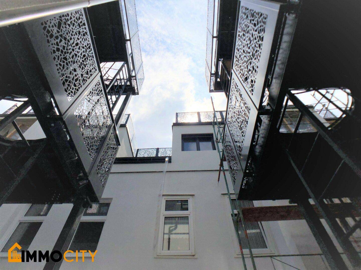 Blick nach oben auf die Balkone mit dekorativen Metallgeländern und die Gebäudefassade.
