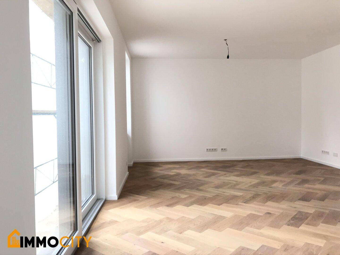 Heller, leerer Raum mit Fischgrätparkett und großer Fenstertür, ideal für den Wohnbereich.