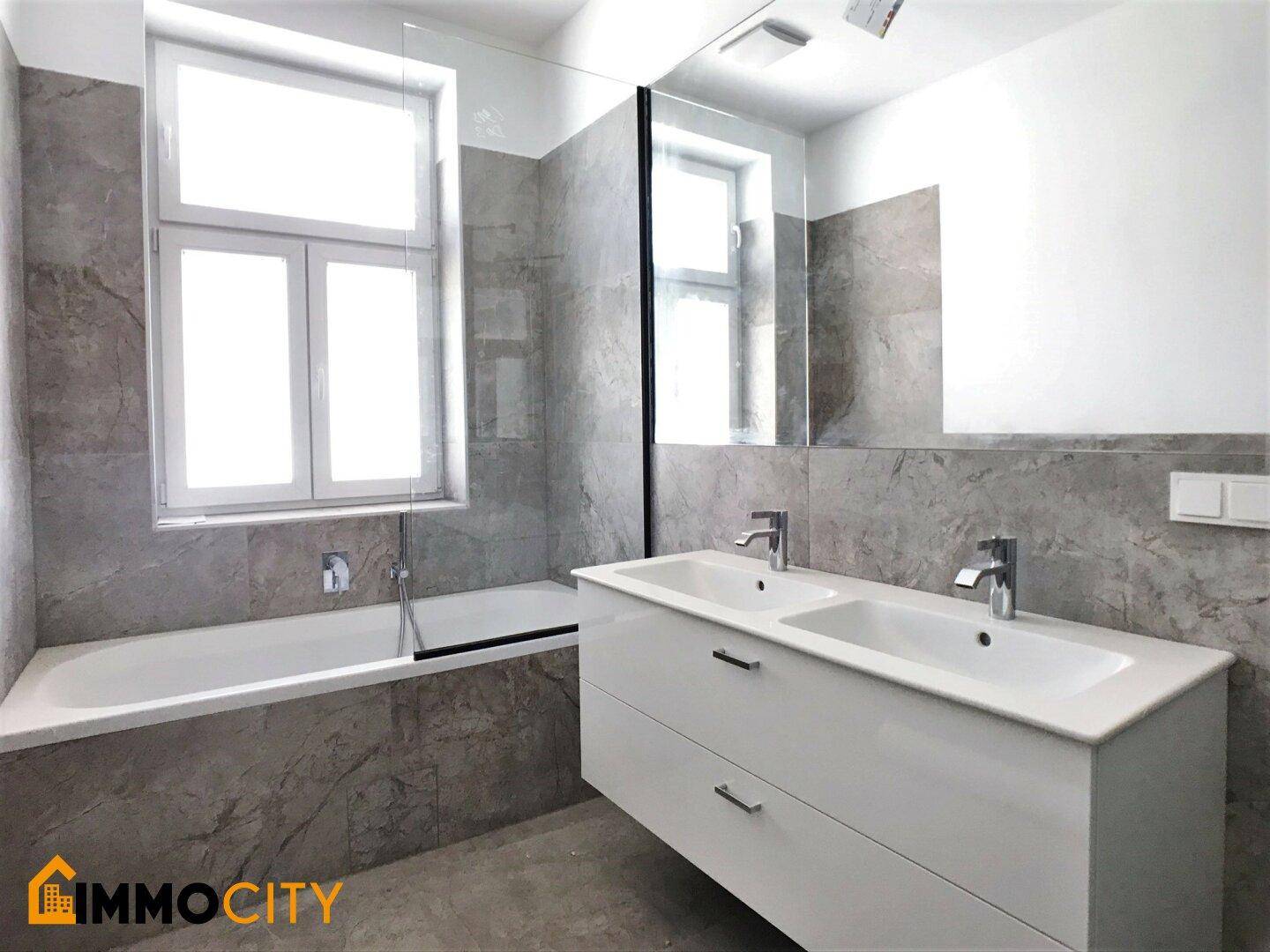 Modernes Badezimmer mit Doppelwaschbecken, Badewanne und eleganten grauen Marmorfliesen an den Wänden.