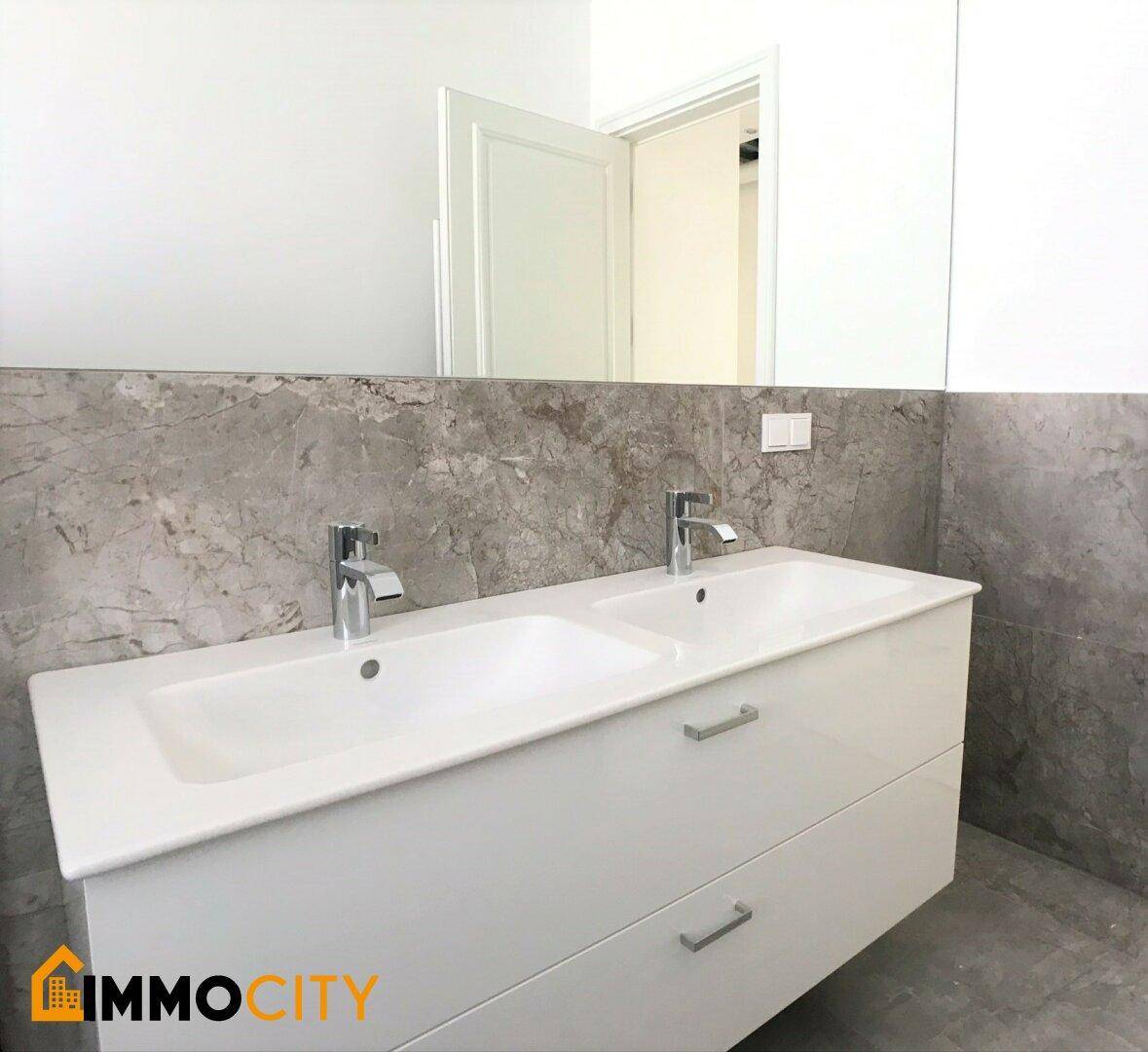 Modernes Badezimmer mit Doppelwaschbecken und großem Spiegel über Marmorfliesen an der Wand.