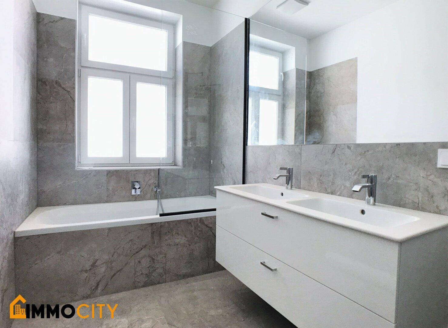 Modernes Badezimmer mit Doppelwaschbecken, Badewanne und grauen Marmorfliesen an den Wänden.