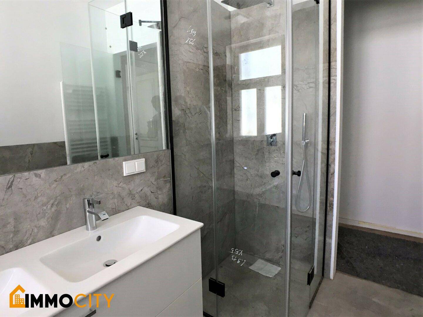 Modernes Badezimmer mit begehbarer Dusche, eleganten grauen Fliesen und einem Waschbecken.