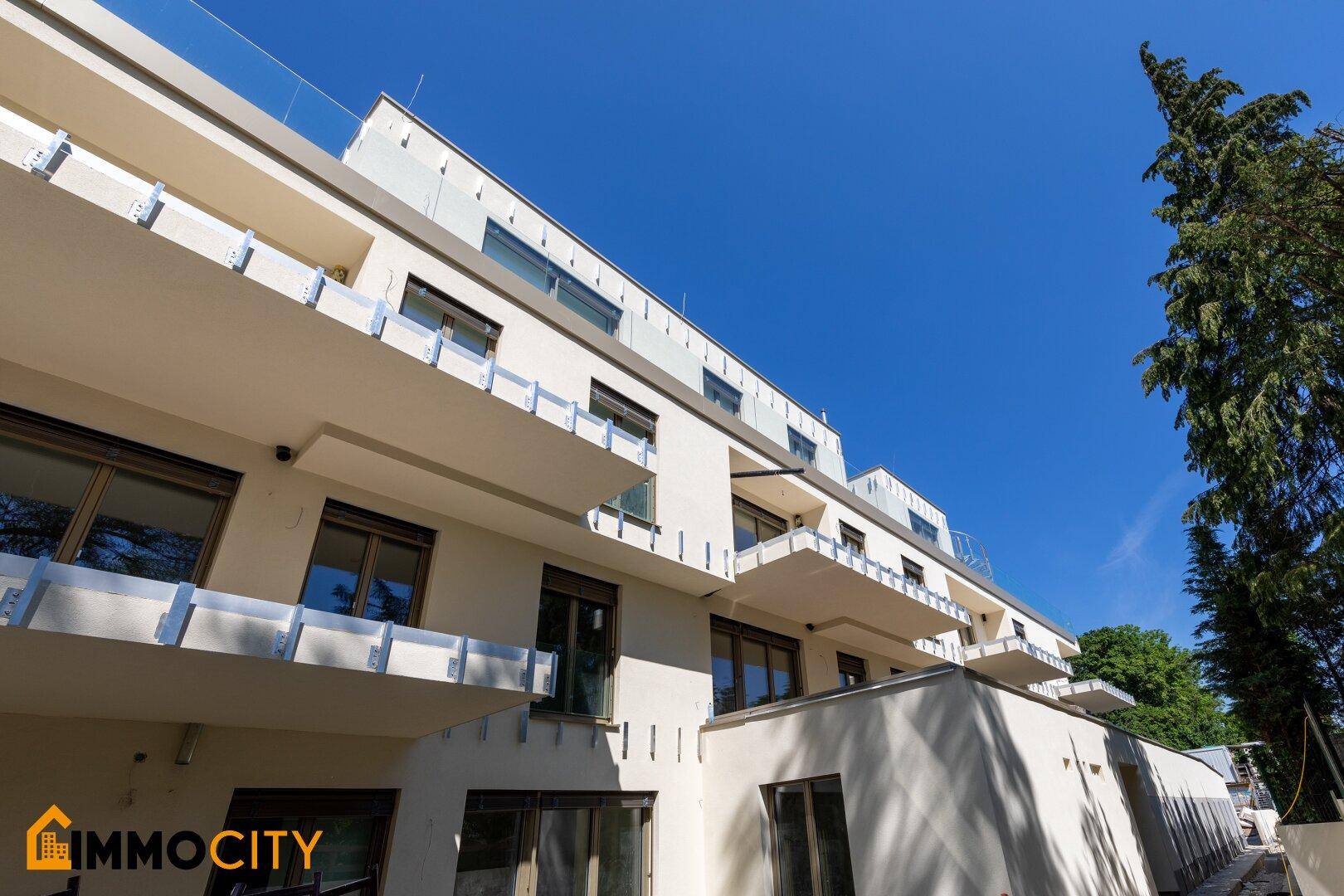 Moderne Wohnanlage mit mehreren Balkonen und heller Fassade unter blauem Himmel.