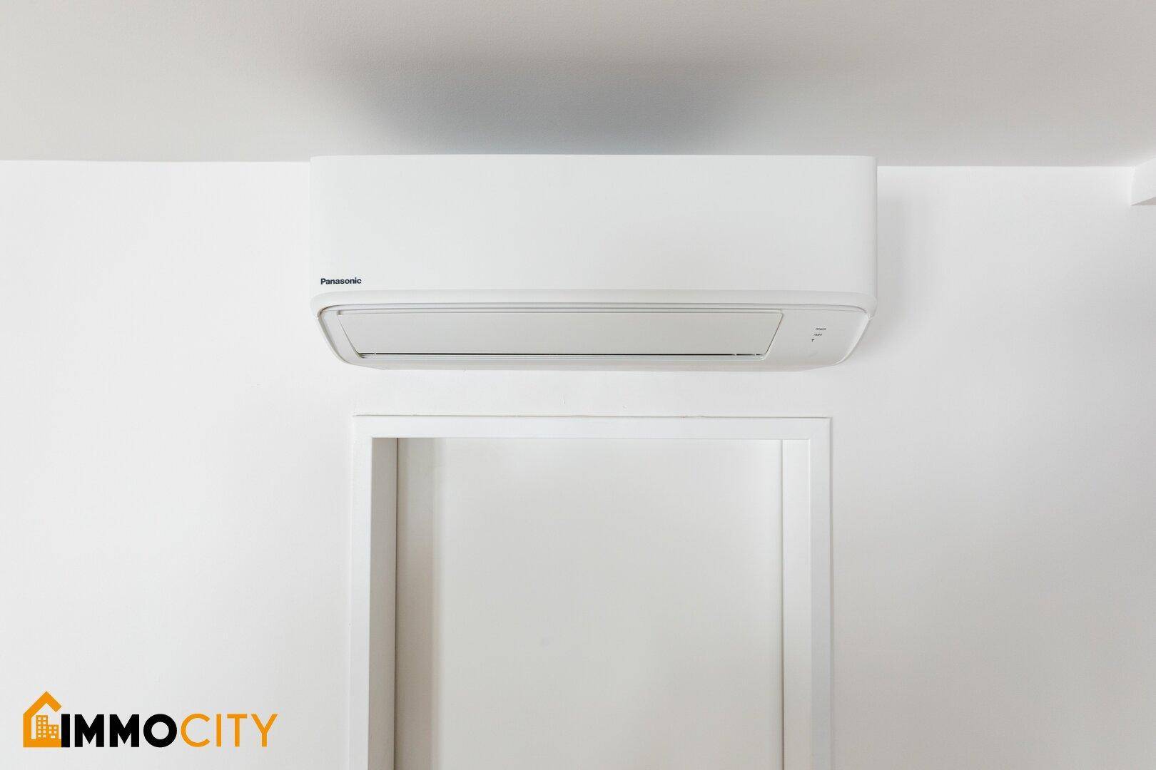 Weiße Klimaanlage an einer hellen Wand über einem Türrahmen in einem modernen Innenraum.