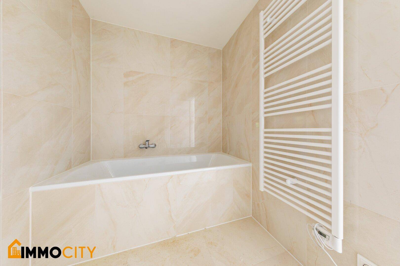 Modernes Badezimmer mit beigefarbenen Fliesen, Badewanne und beheiztem Handtuchhalter.