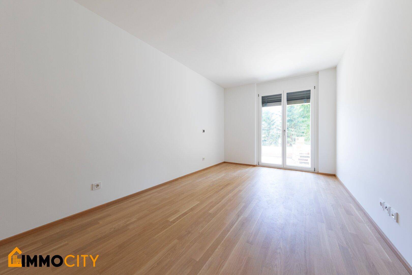 Helles Schlafzimmer mit Parkettboden und Fenster mit Rollläden für Privatsphäre.