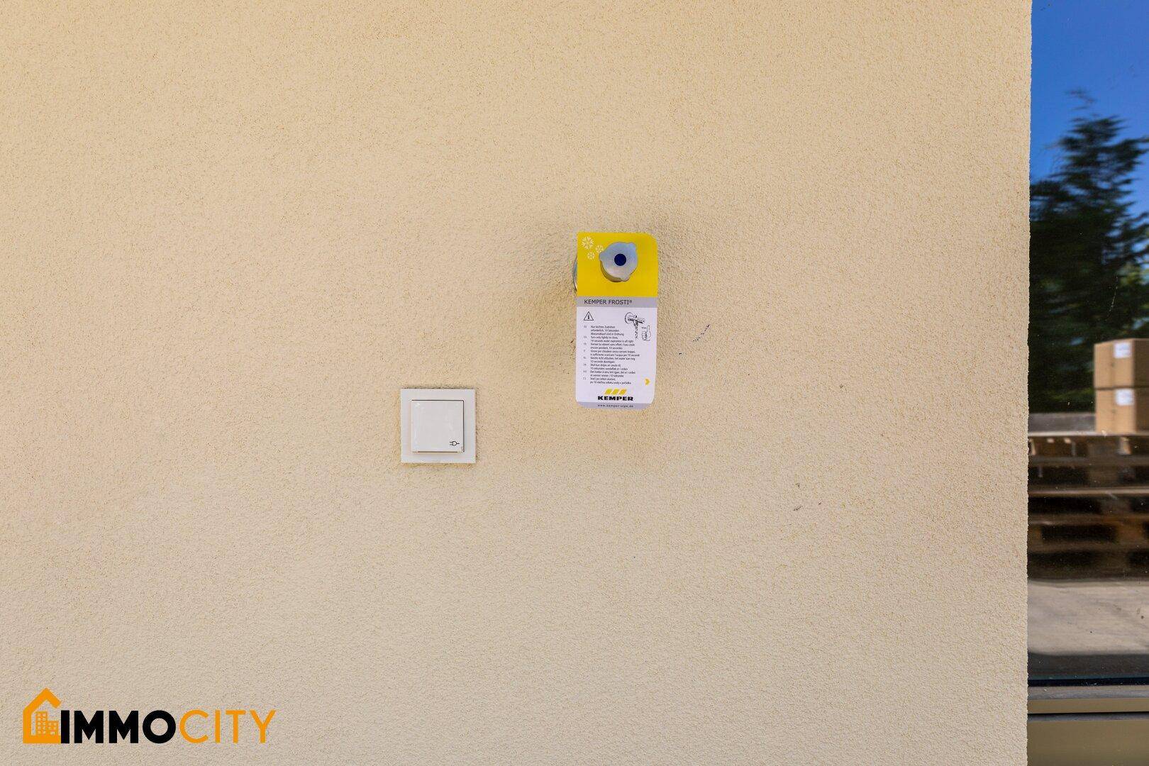 Detailansicht einer hellen Außenwand mit Lichtschalter und einer technischen Box.