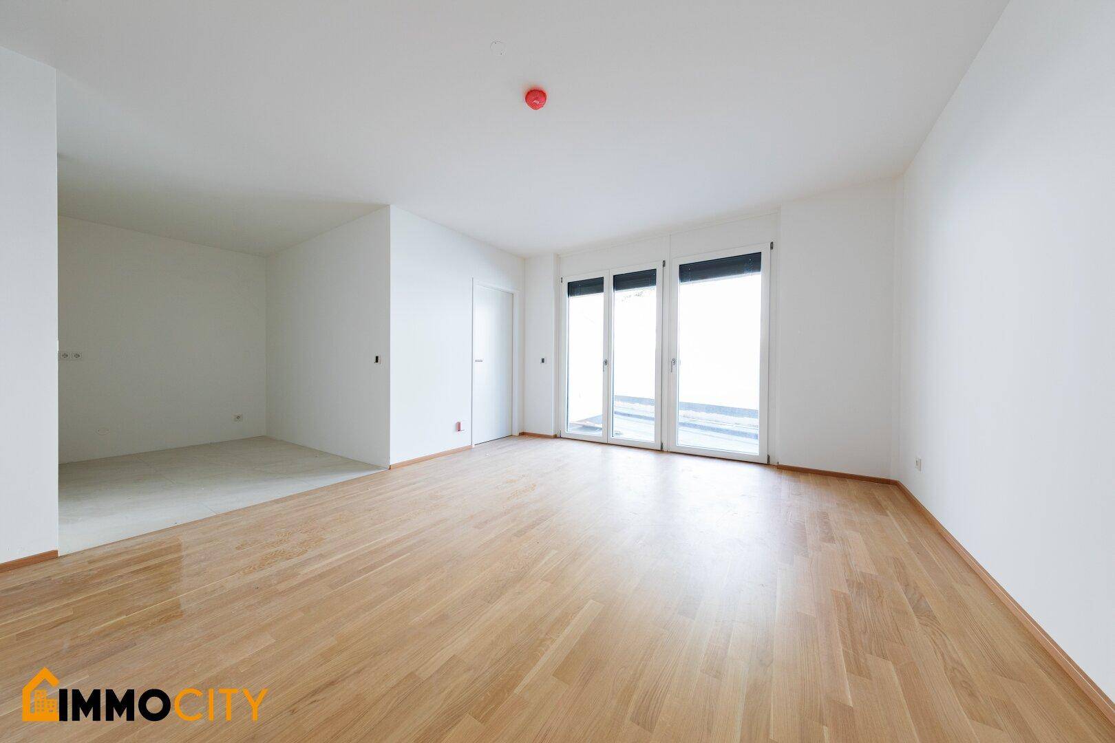 Großer, heller Wohnbereich mit Parkettboden und Zugang zu einem weiteren Zimmer.