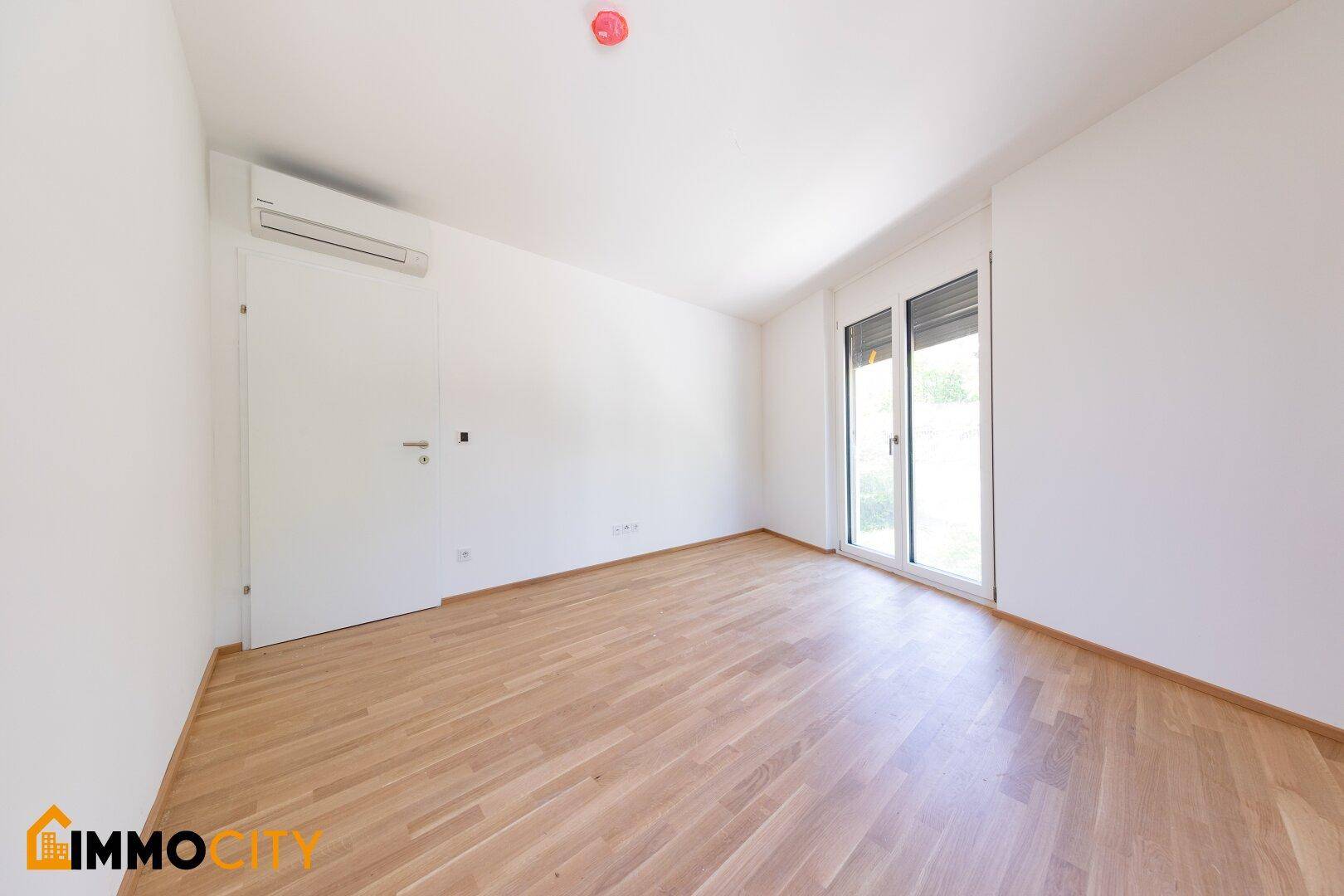 Helles Schlafzimmer mit Parkettboden, Klimaanlage und Zugang zu einem Außenbereich.