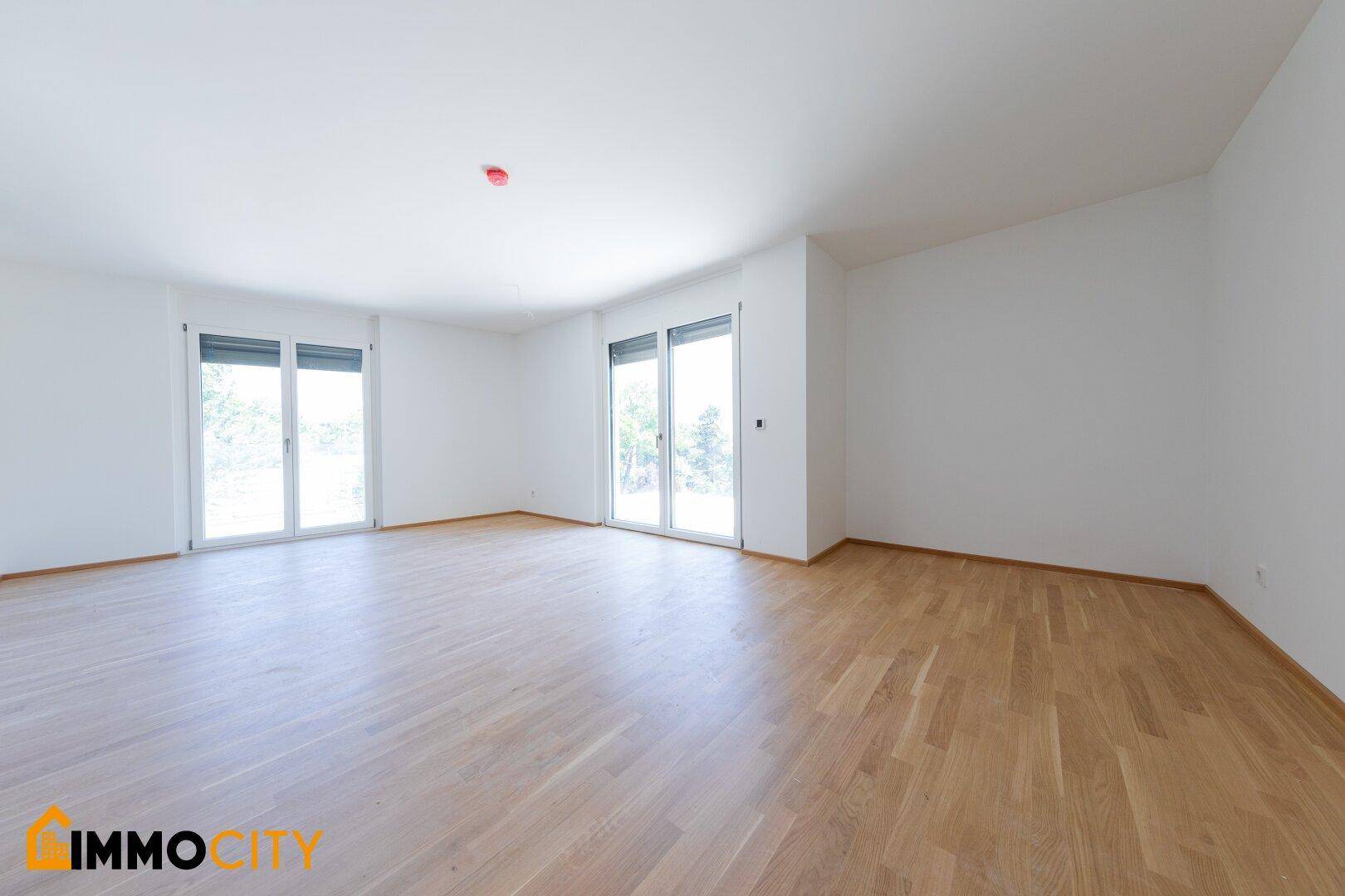 Geräumiger, heller Wohnbereich mit Parkettboden und zwei großen Fenstern für viel Licht.