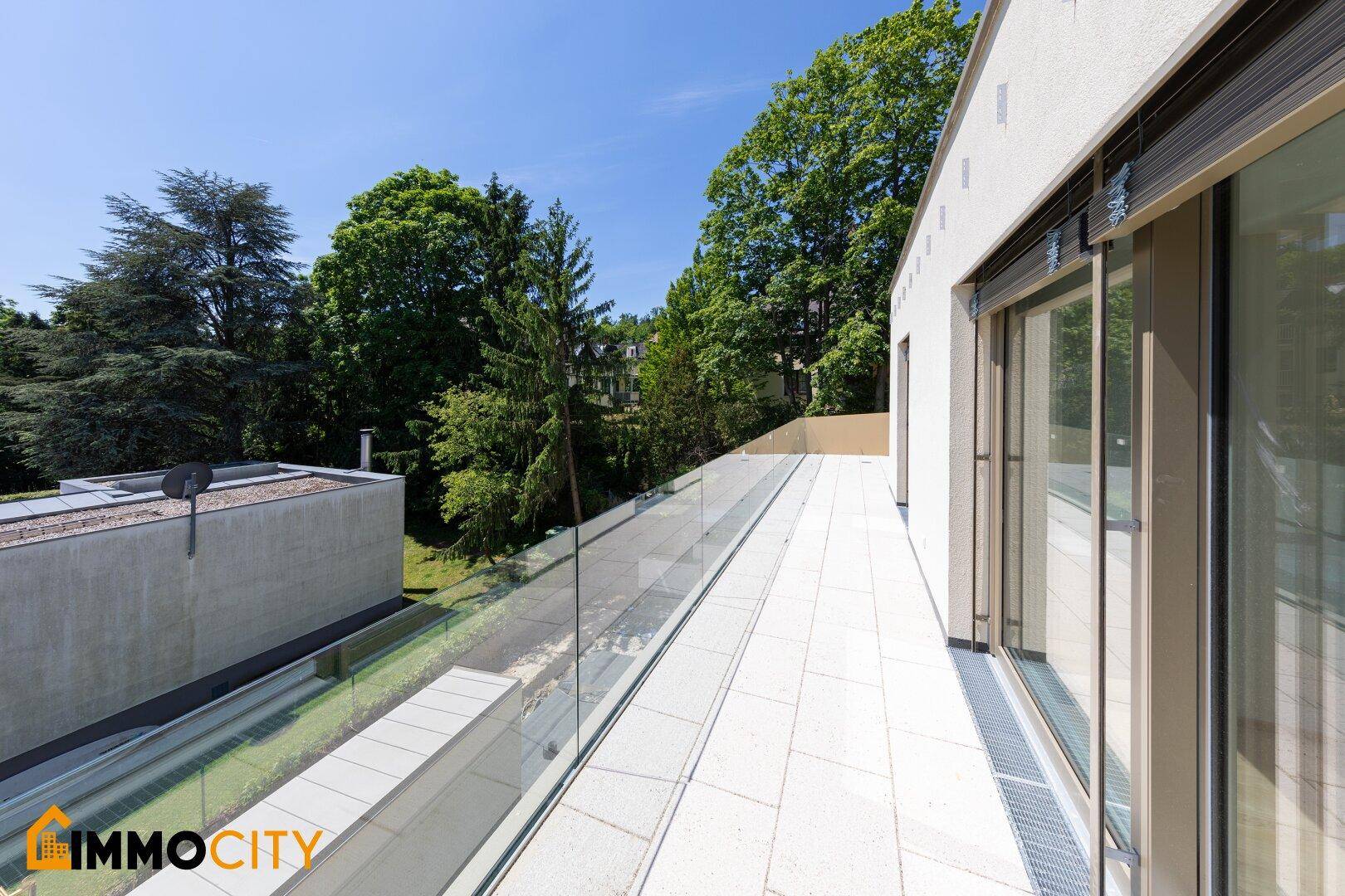 Langer, schmaler Terrassenbereich mit Glasgeländer und Blick ins Grüne.