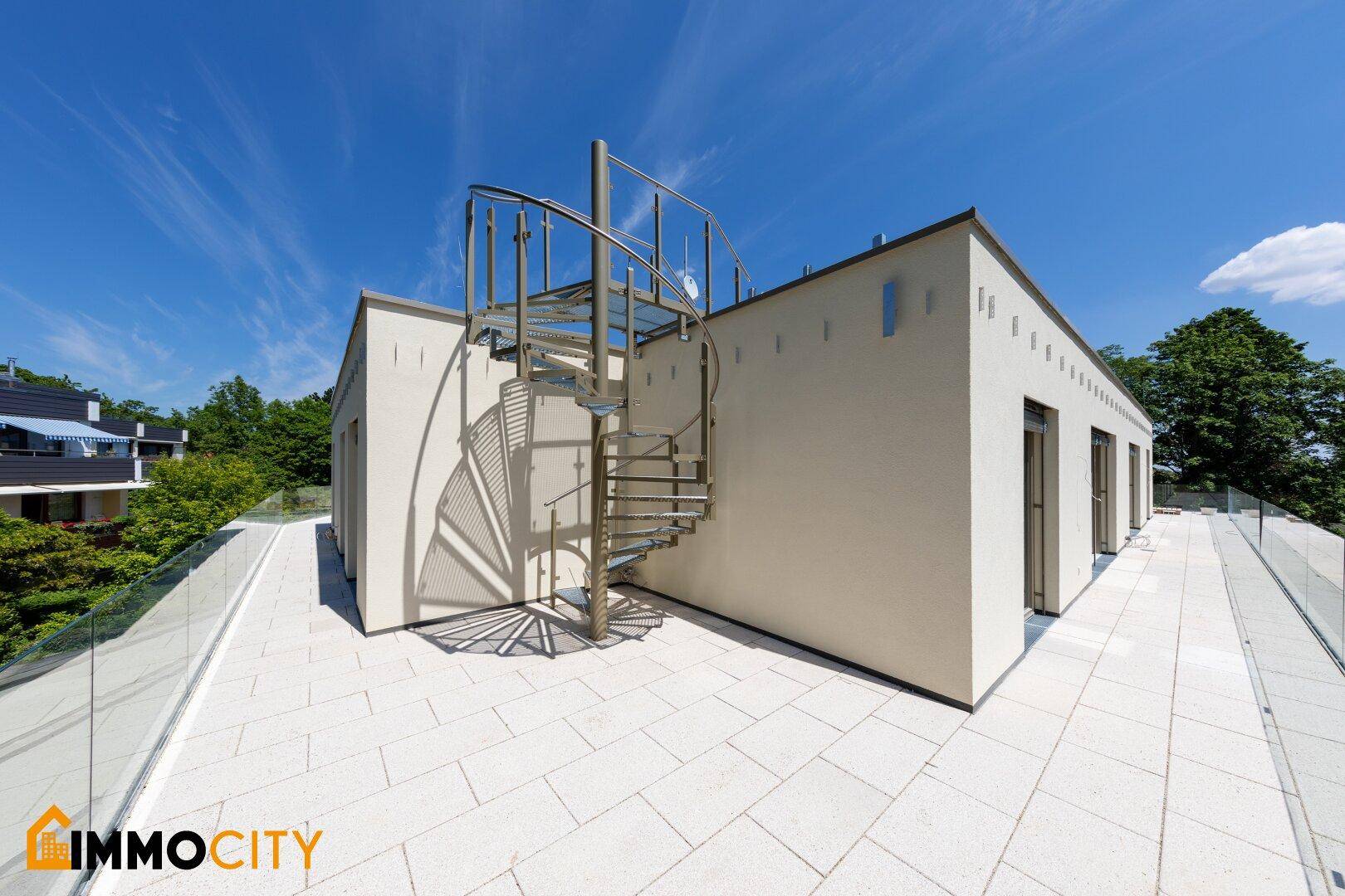 Große Dachterrasse mit Steinplatten und eleganter Wendeltreppe unter strahlendem Himmel.
