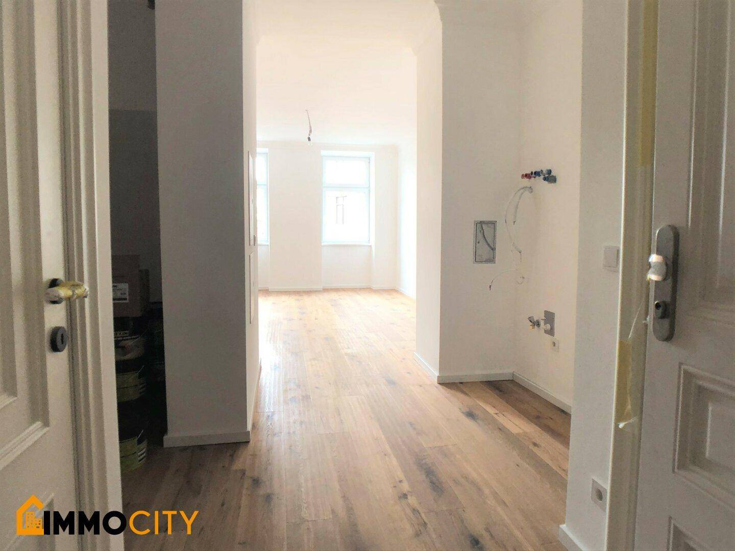 Heller Eingangsbereich mit Holzboden und Blick in weitere Zimmer, teilweise mit Installationsvorbereitungen.