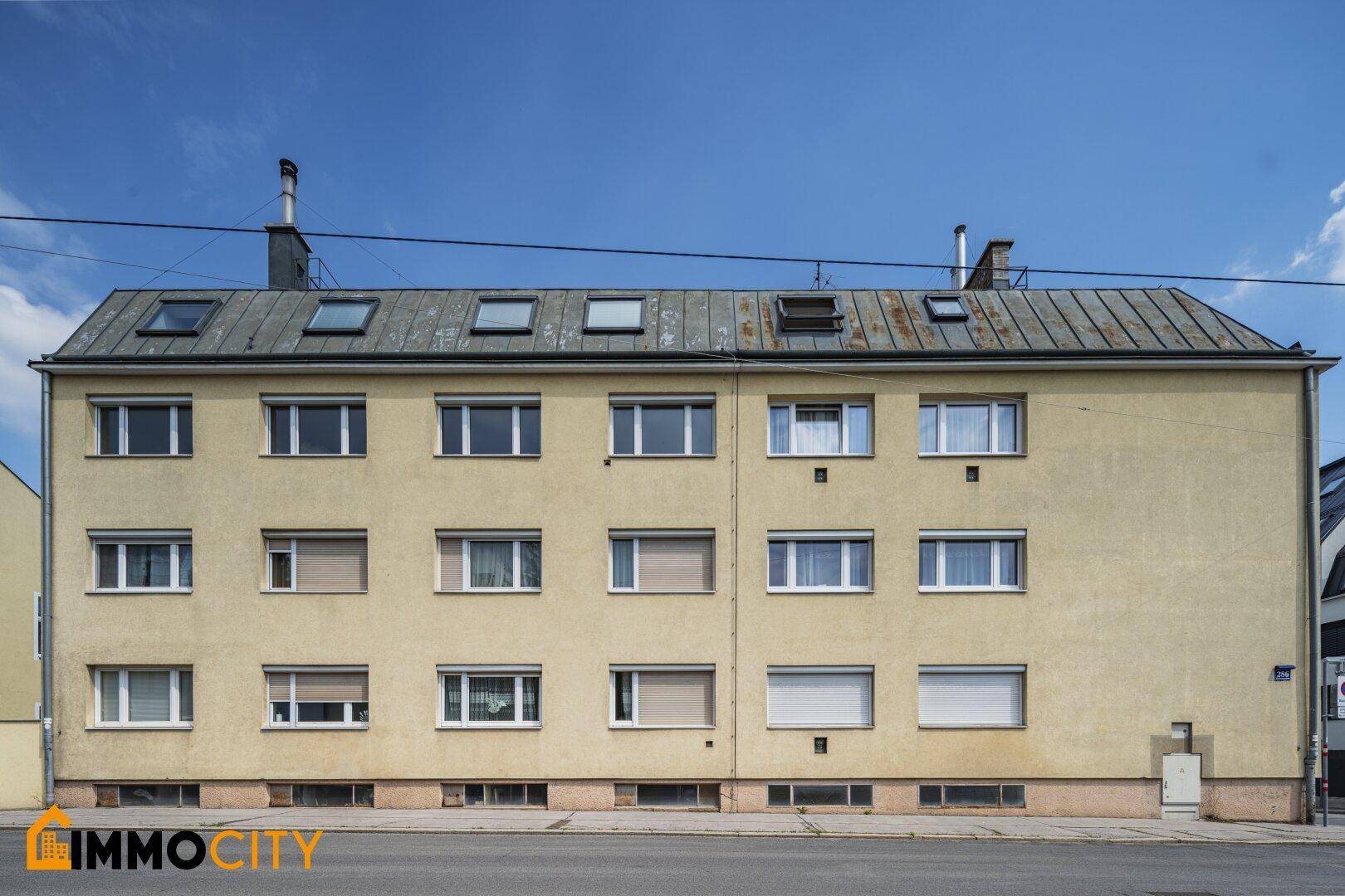 Klassische Fassade eines Mehrfamilienhauses mit zahlreichen Fenstern und einem Metall-Dach.