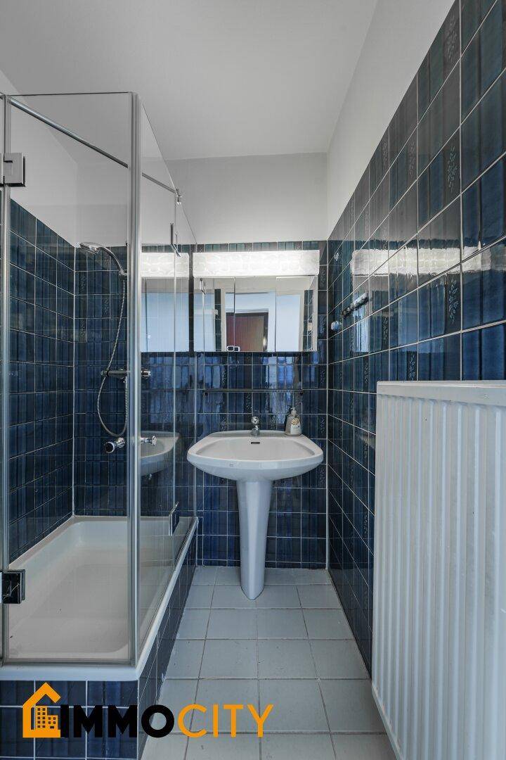 Badezimmer mit dunkelblauen Fliesen, Dusch-Badewannen-Kombination und Waschtisch mit Spiegelschrank.