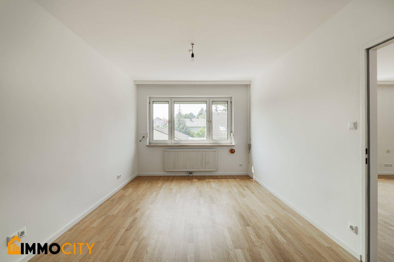 Helles Schlafzimmer mit Parkettboden und einem großen Fenster, das für eine freundliche Atmosphäre sorgt.